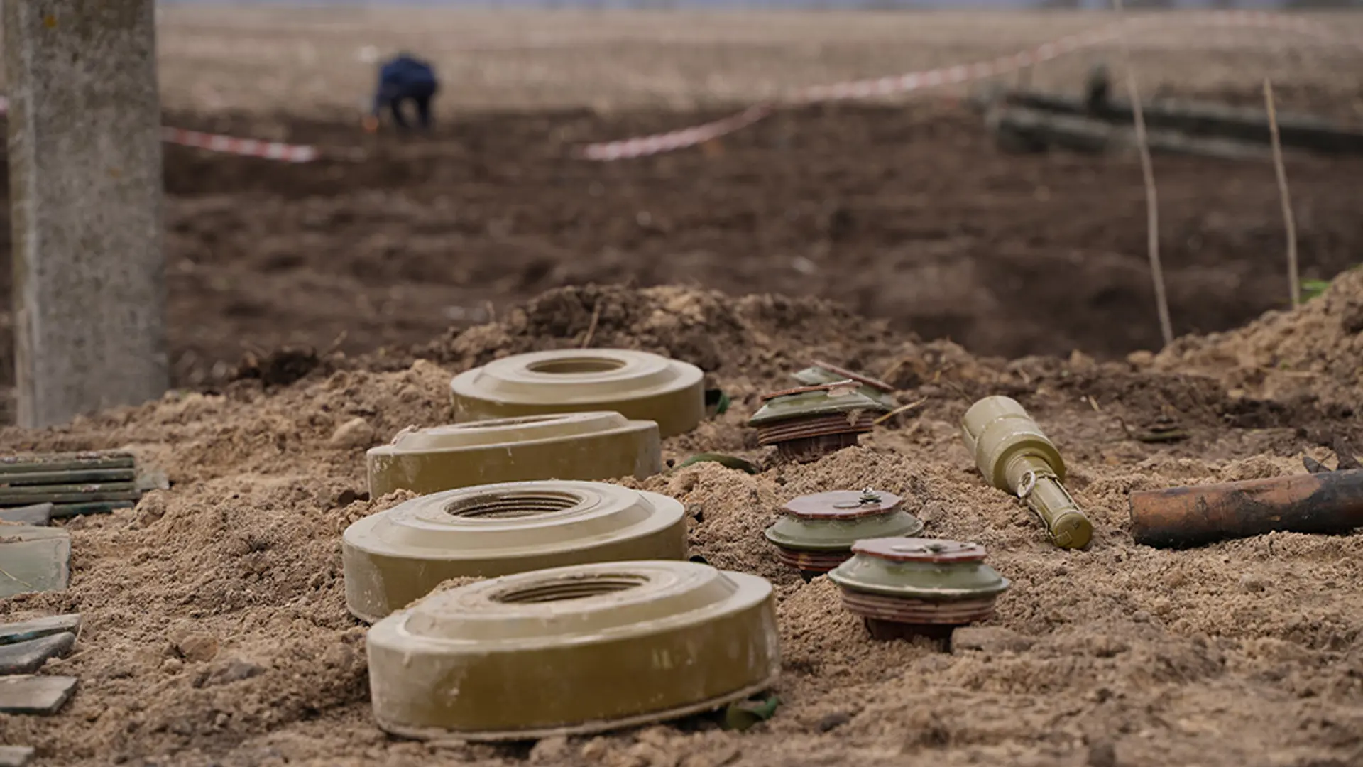Deactivated anti-tank mines lined up beside a cleared minefield for safe disposal.