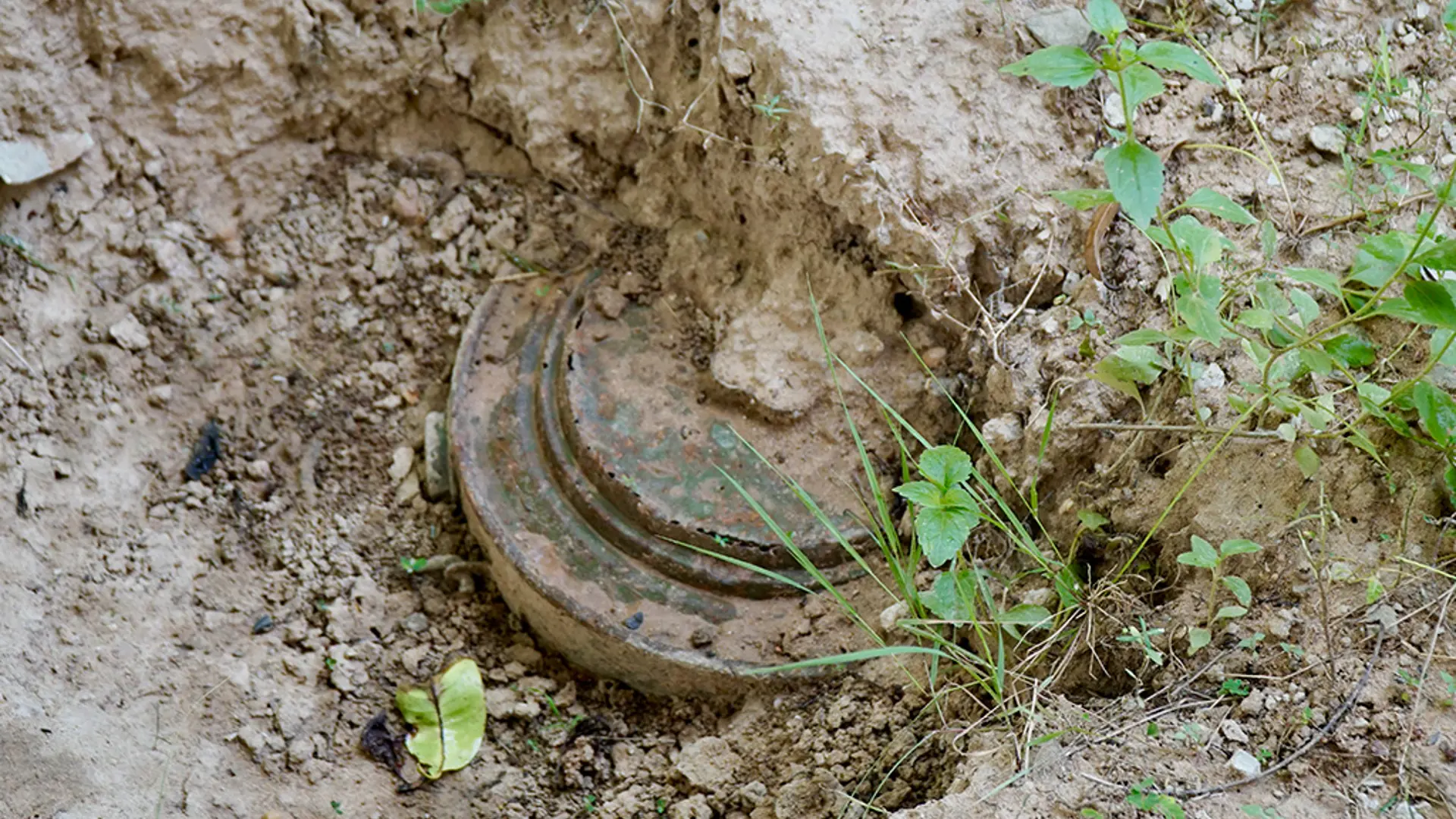 Rusting anti-tank landmine partially buried under layers of mud in a hazardous area.
