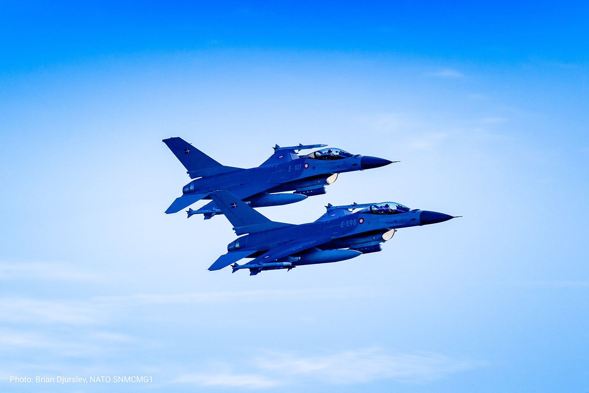Two NATO F-16 fighter jets in tight formation flight against a clear blue sky, demonstrating aerial precision and alliance airpower.