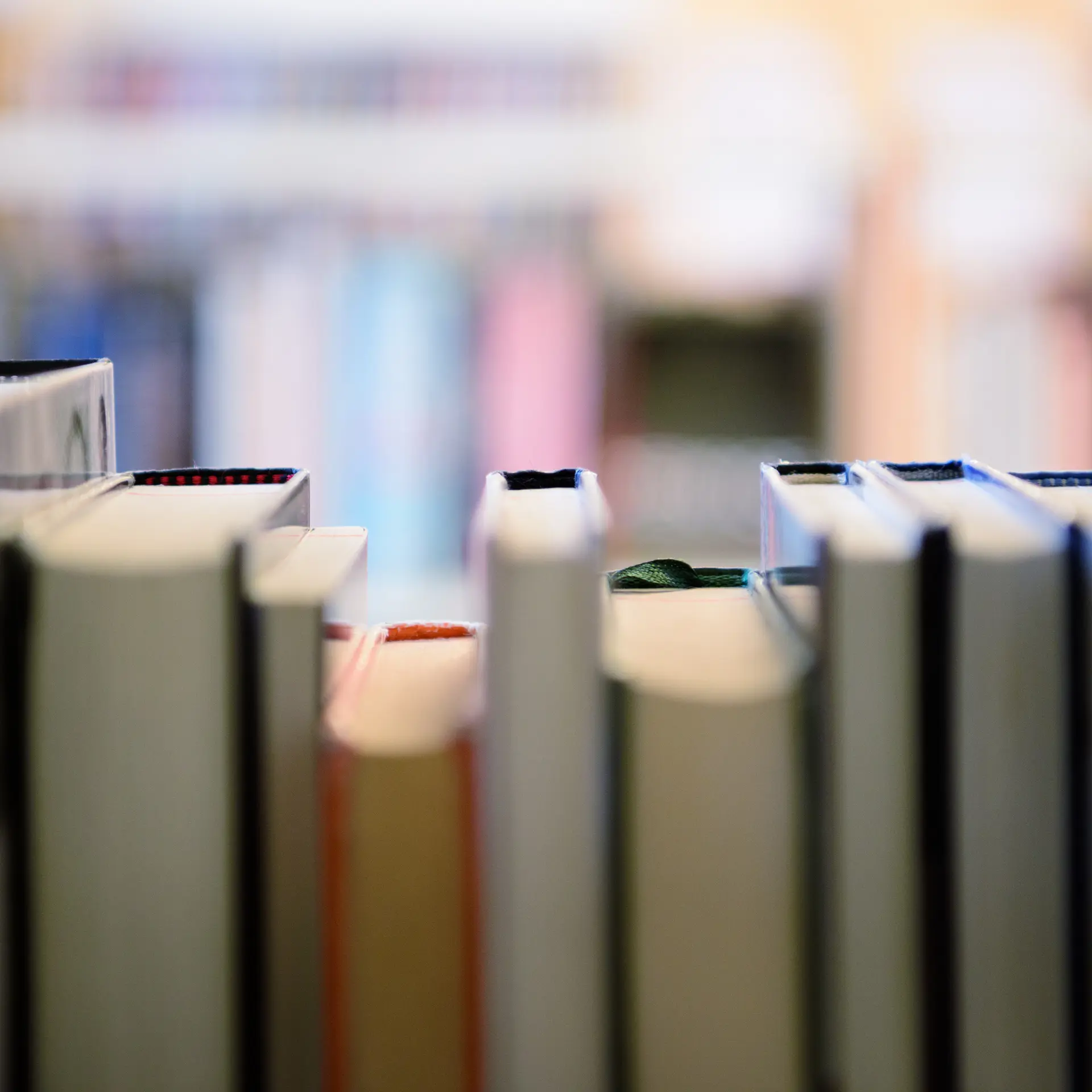 Close-up view from inside a library bookshelf showing the spines and tops of various books, with blurred shelves in the background.