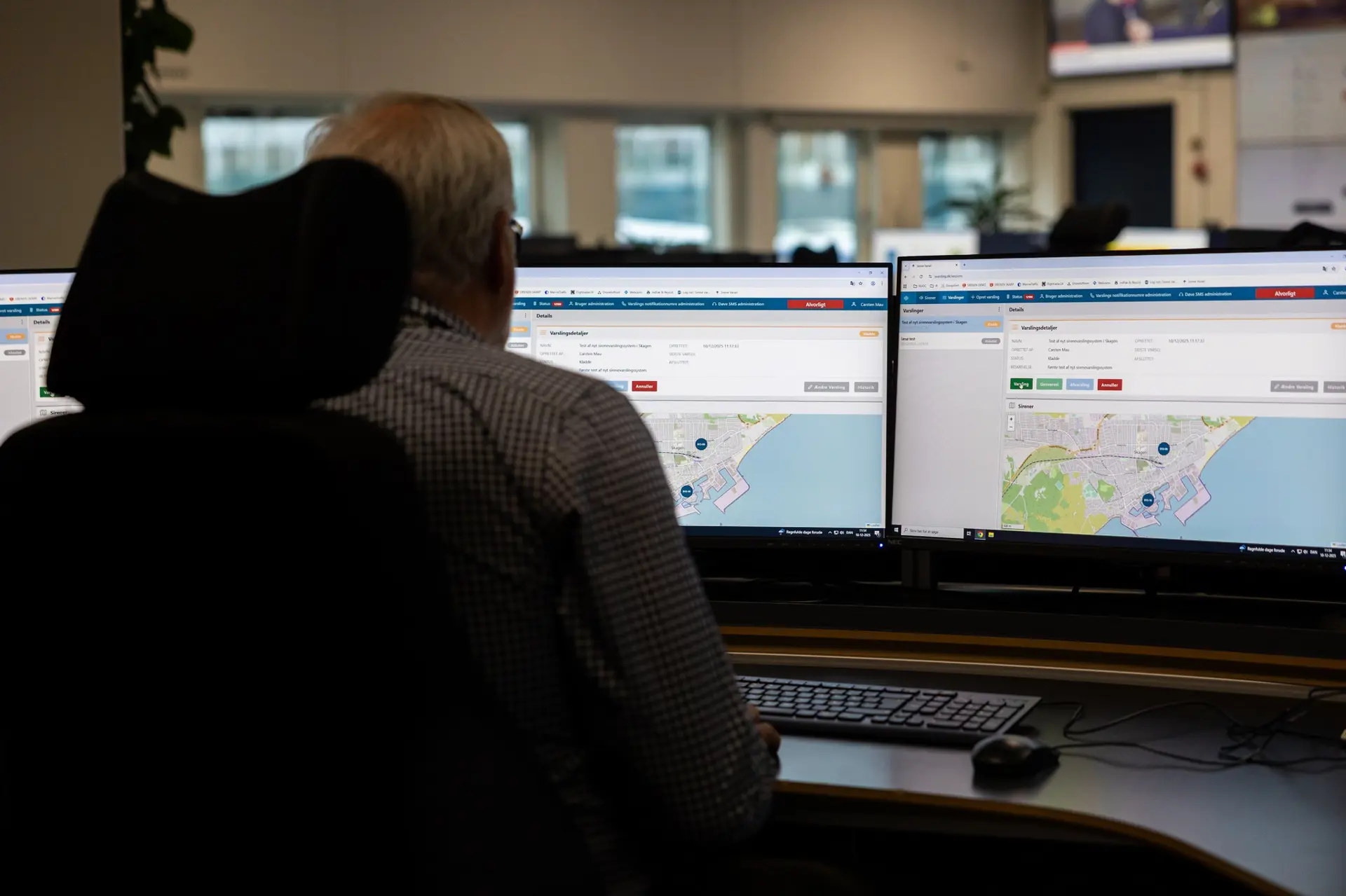 Person at a workstation viewing Systematic's siren warning system on two monitors, with a map and alert details displayed.