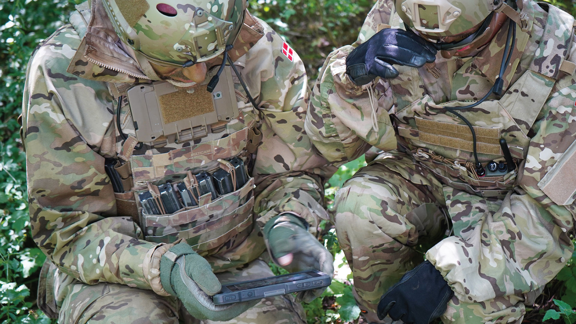 Zwei Soldaten in Tarnuniformen knien im Gelände und analysieren taktische Informationen auf einem robusten Tablet mit dem mobilen Führungs- und Einsatzsystem SitaWare Edge.