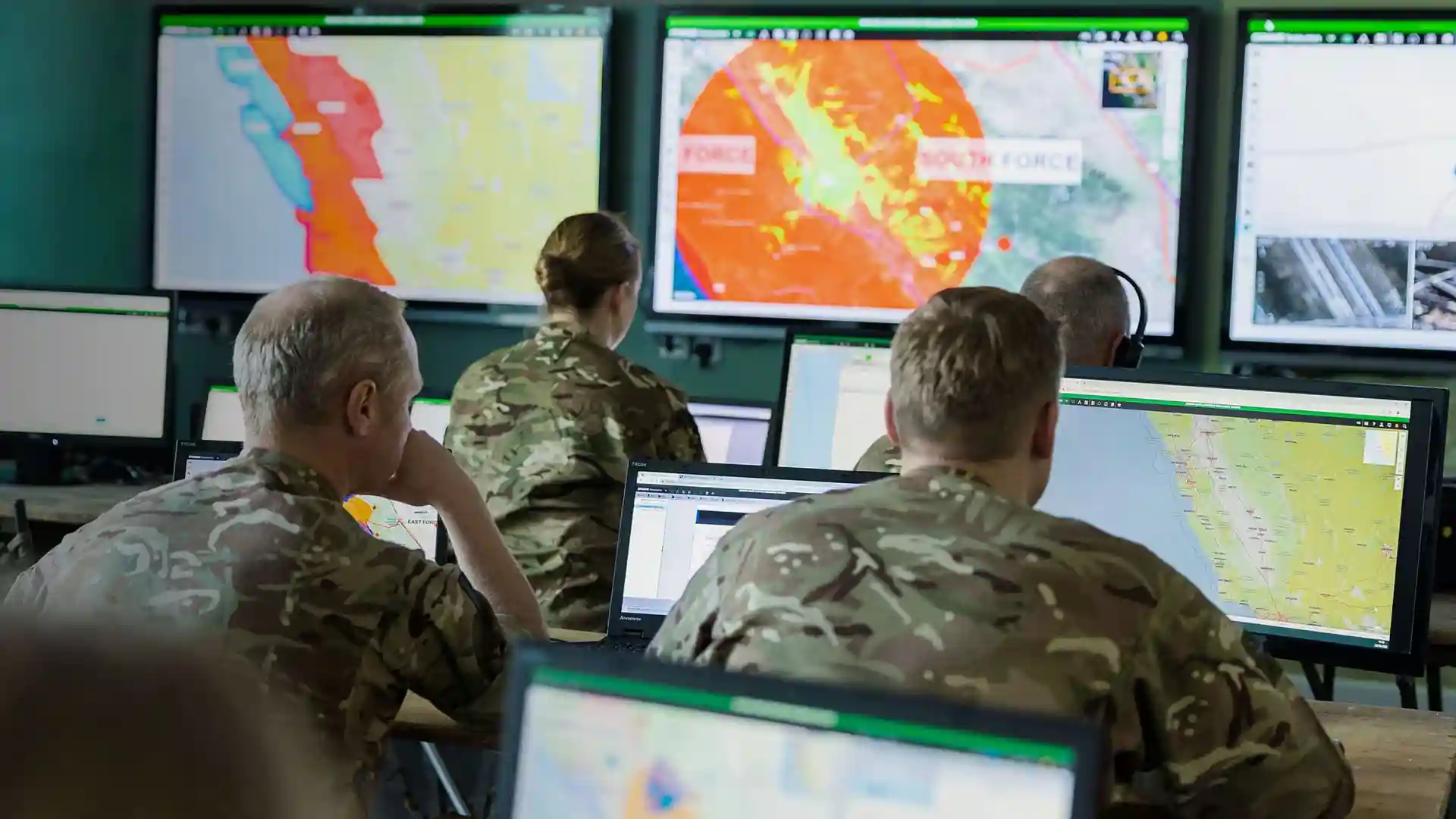 Soldiers in camouflage uniforms monitoring tactical maps and digital intel on multiple screens in a military operations center, using SitaWare Headquarters.