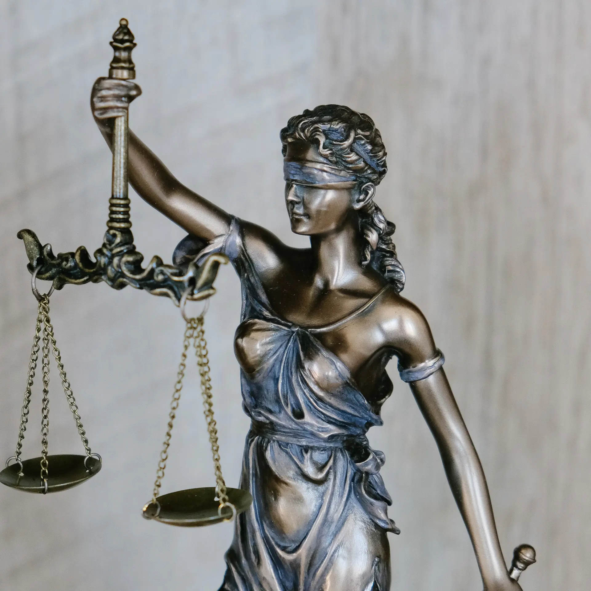 Bronze statue of Lady Justice holding scales, symbolizing fairness and impartiality, with a blurred background of wooden texture."