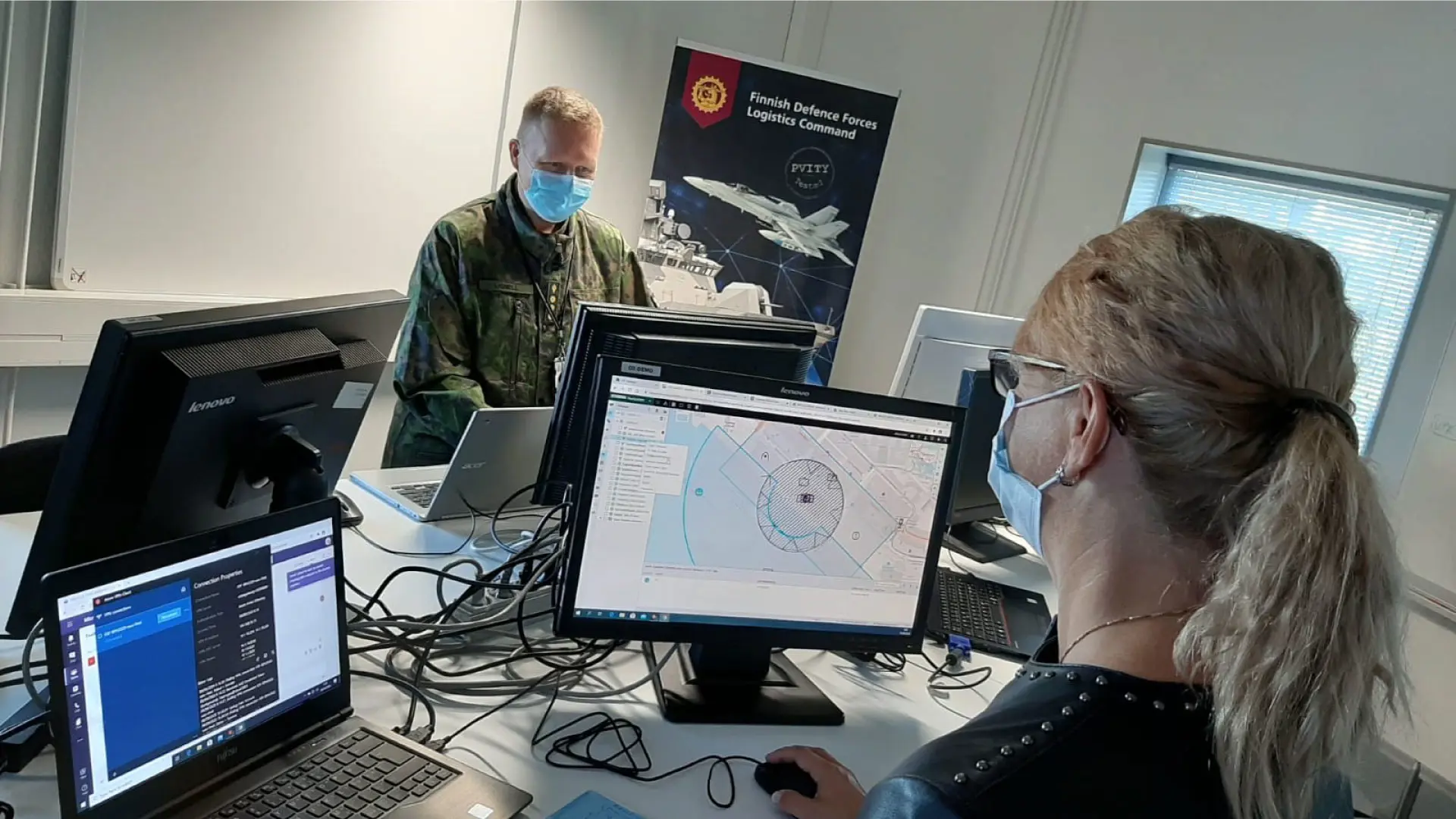Personnel wearing masks work on defense software at computers in a Finnish Defence Forces logistics command setting.