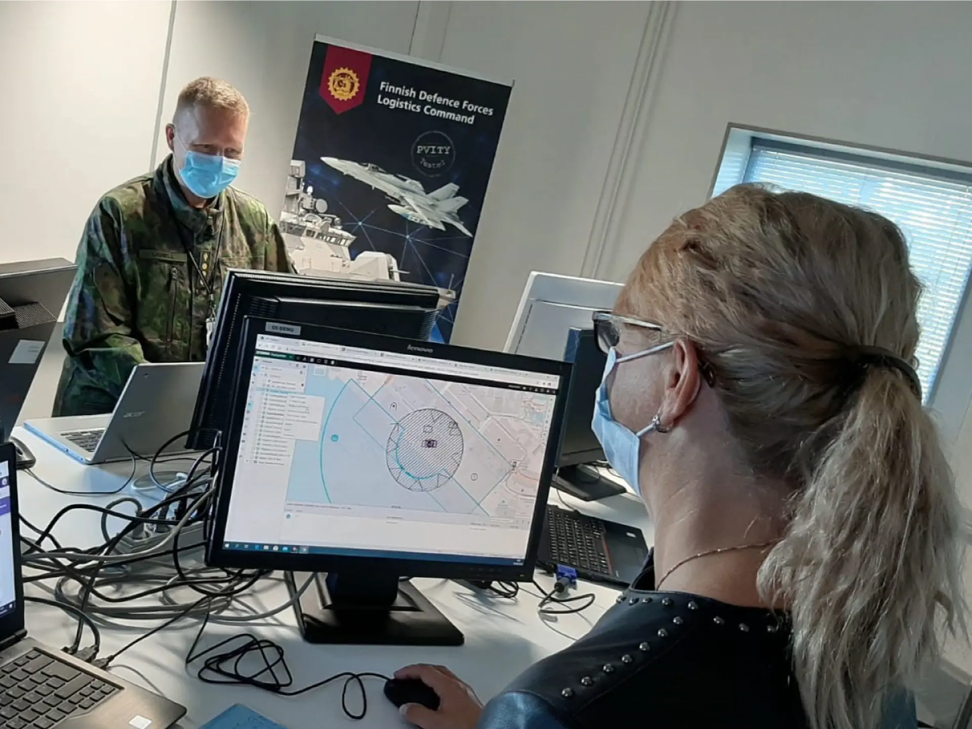 Personnel wearing masks work on defense software at computers in a Finnish Defence Forces logistics command setting.