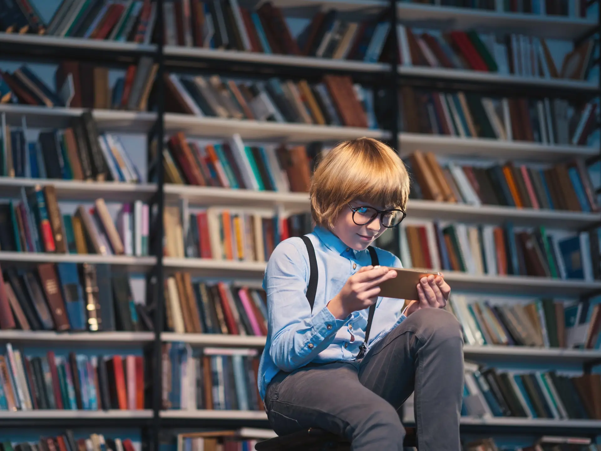 Ung gutt bruker smarttelefon i et bibliotek