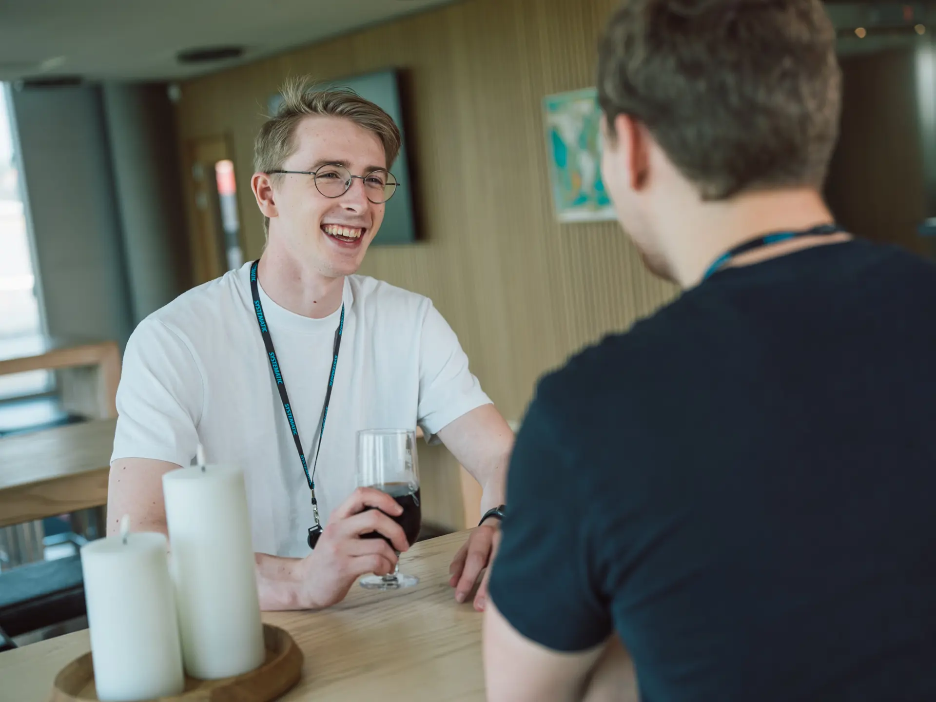 Two Systematic employees enjoying a casual conversation at the Friday Bar, with one holding a drink and smiling in a relaxed, informal setting.