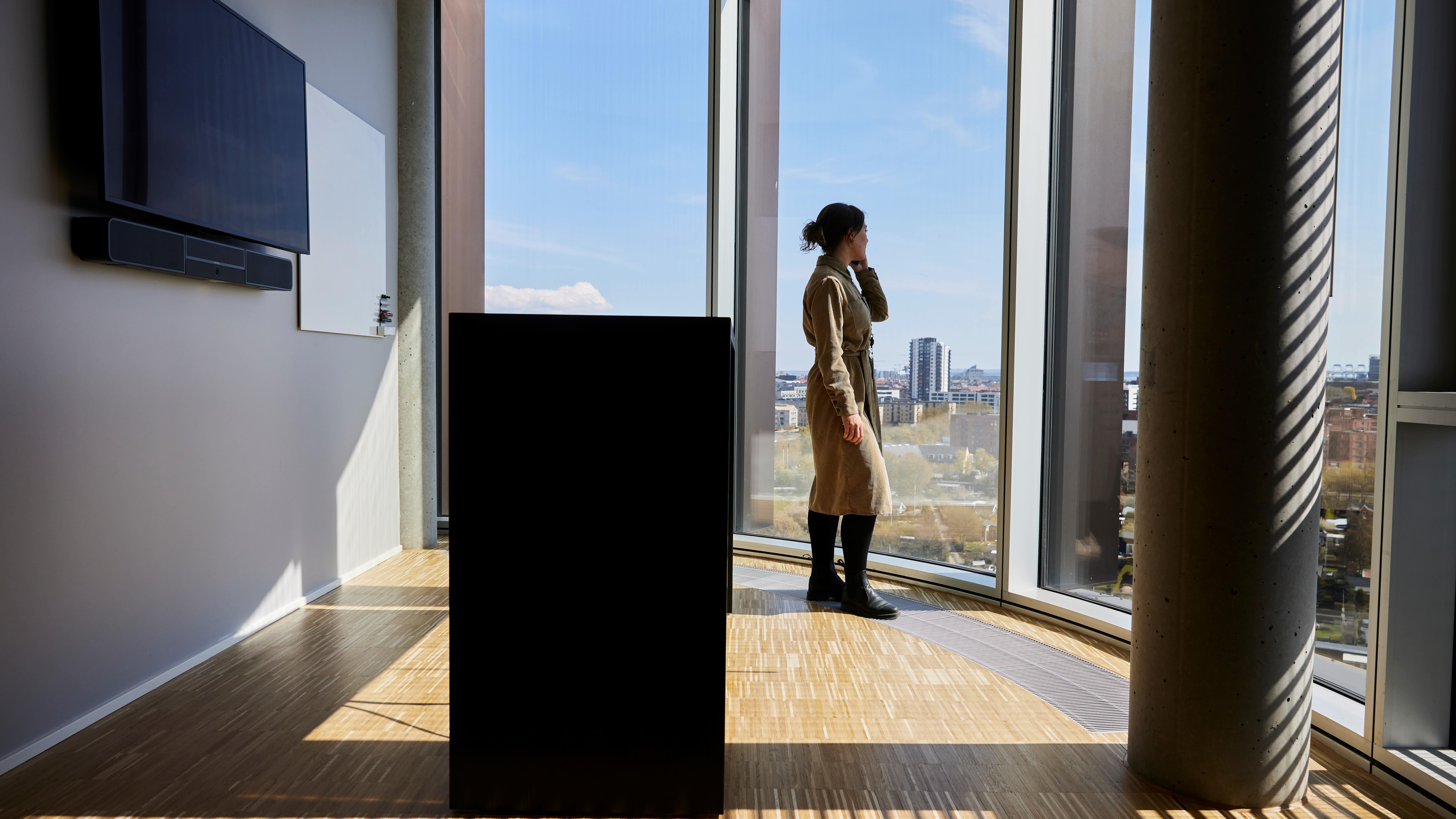 Kvinna pratar i telefon i ett mötesrum på Systematics huvudkontor, stående vid stora fönster med utsikt över staden.