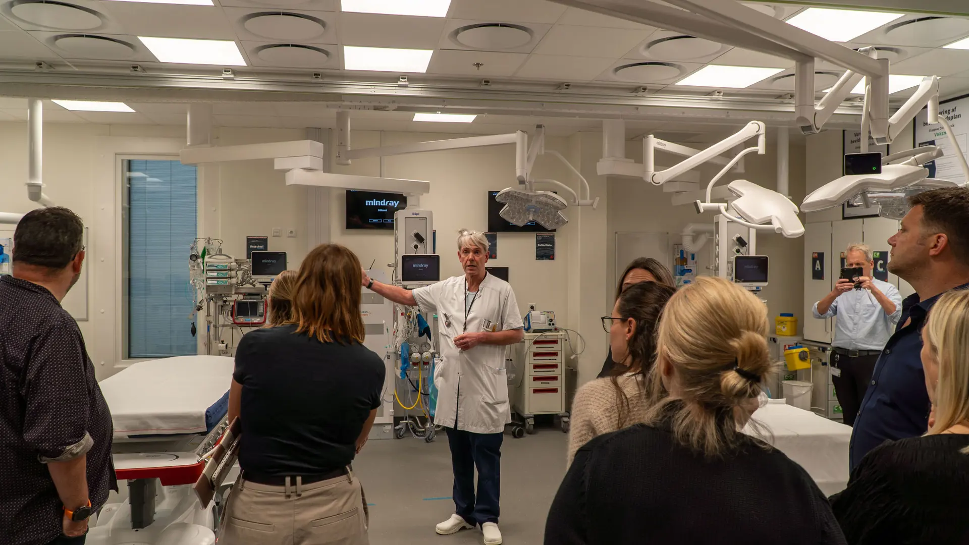 Staff member at Aalborg University Hospital presents to a delegation from Manchester University NHS Foundation Trust in a clinical room with medical equipment.