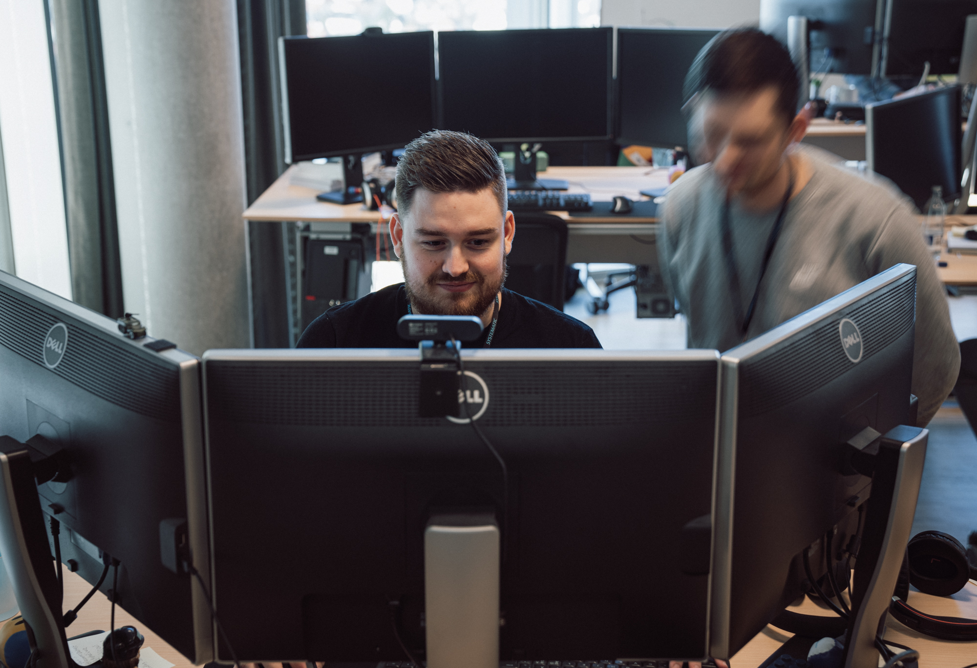 Systematic employees working at headquarters, focused on multiple computer monitors in a modern office environment.