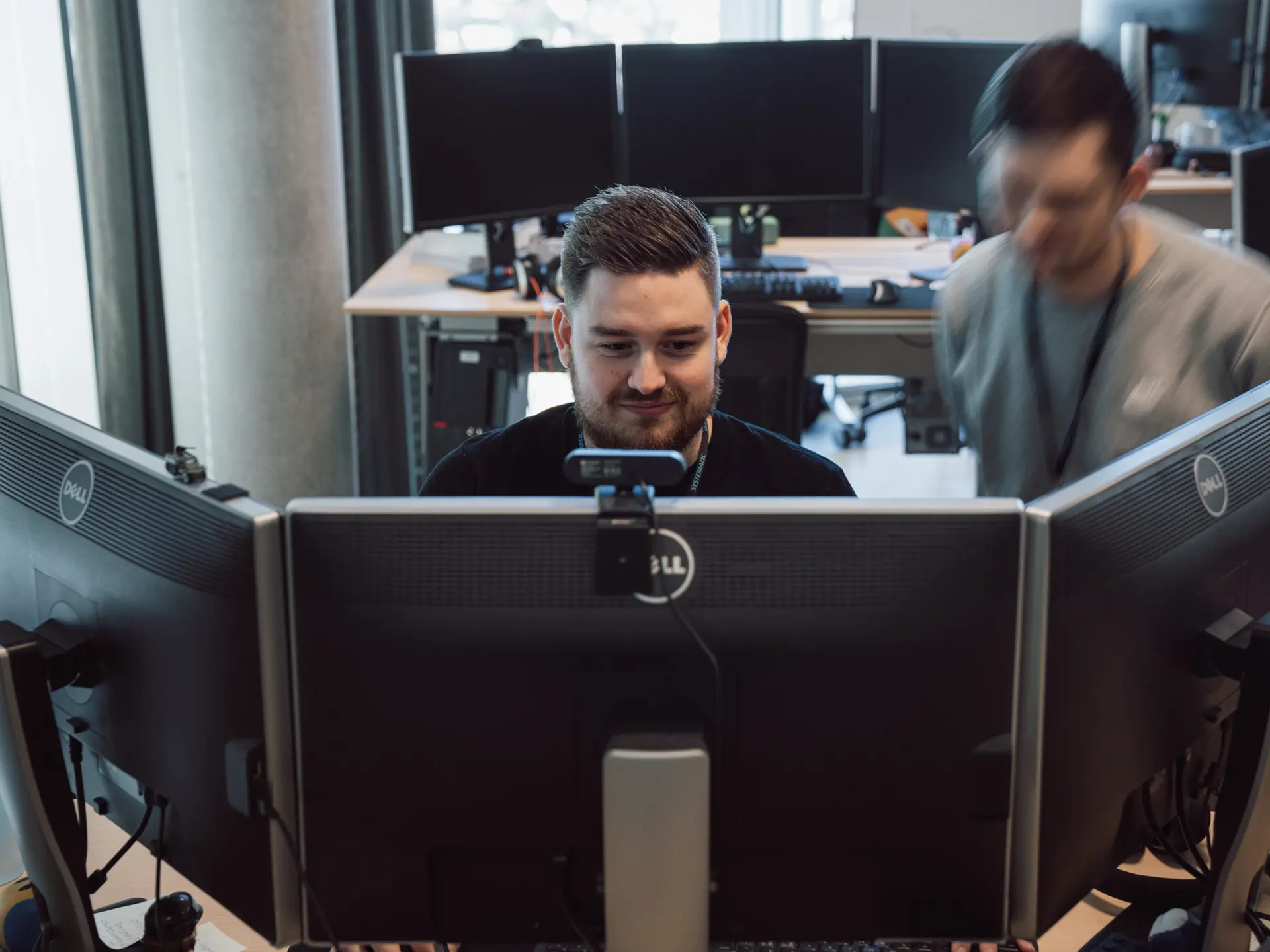 Systematic employees working at headquarters, focused on multiple computer monitors in a modern office environment.