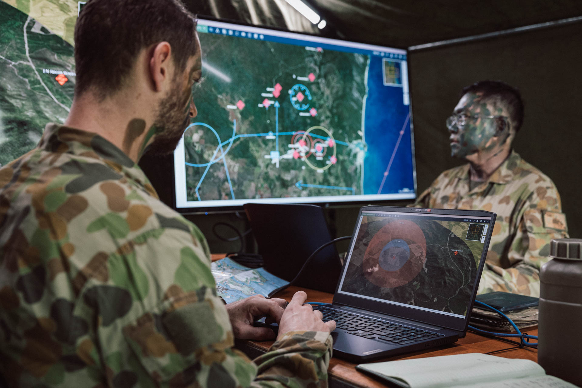 Soldiers monitor tactical maps and live mission data across multiple screens with SitaWare HQ software in a command post.