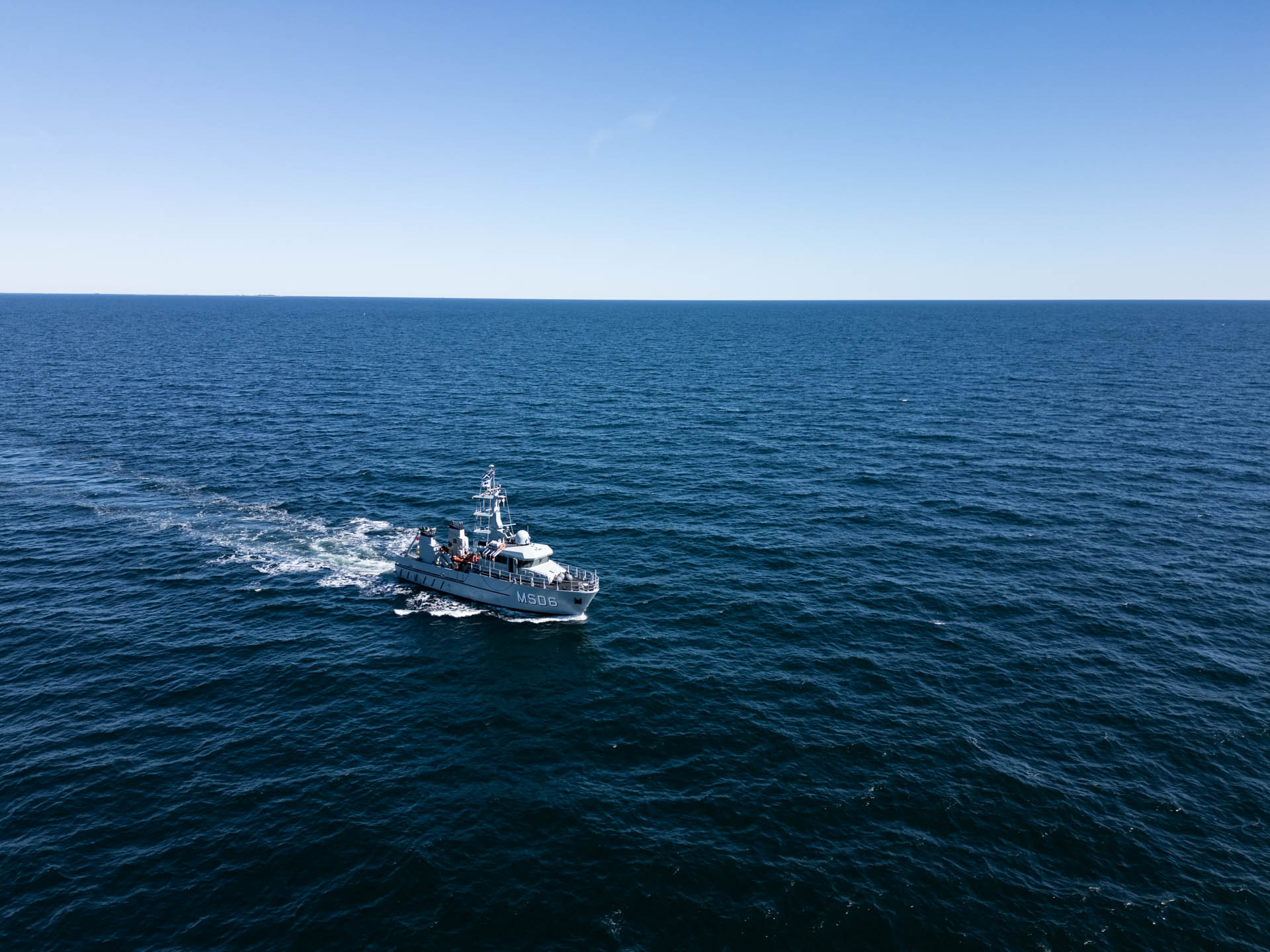 Danish naval vessel MSD6 patrols open water during a mine countermeasures operation, seen from above.