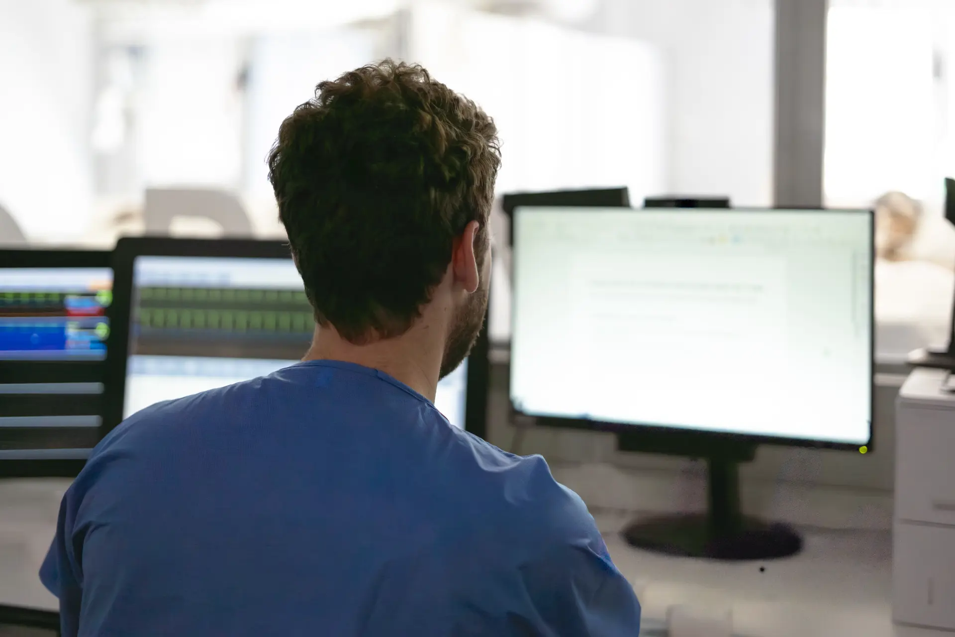 Healthcare professional reviewing clinical data on multiple screens at a hospital workstation.