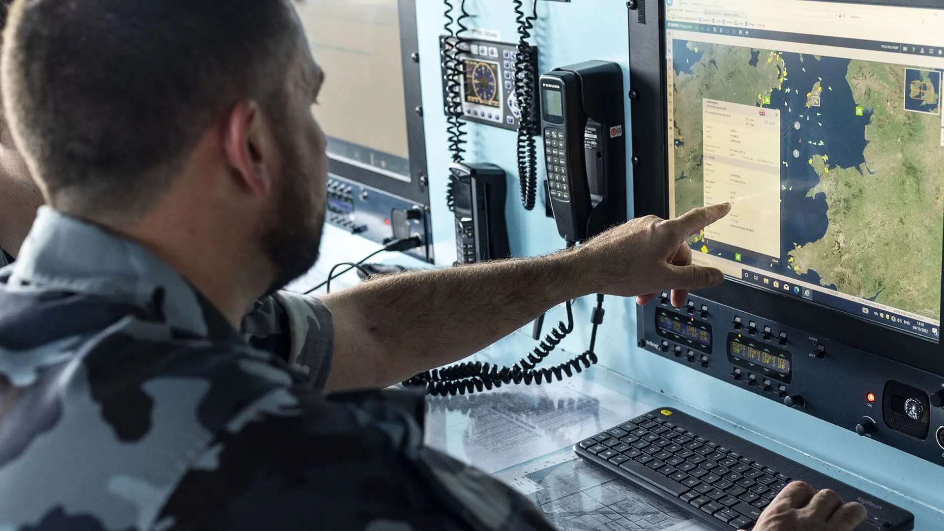 A naval officer in camouflage points at a maritime map on a computer screen in a command centre