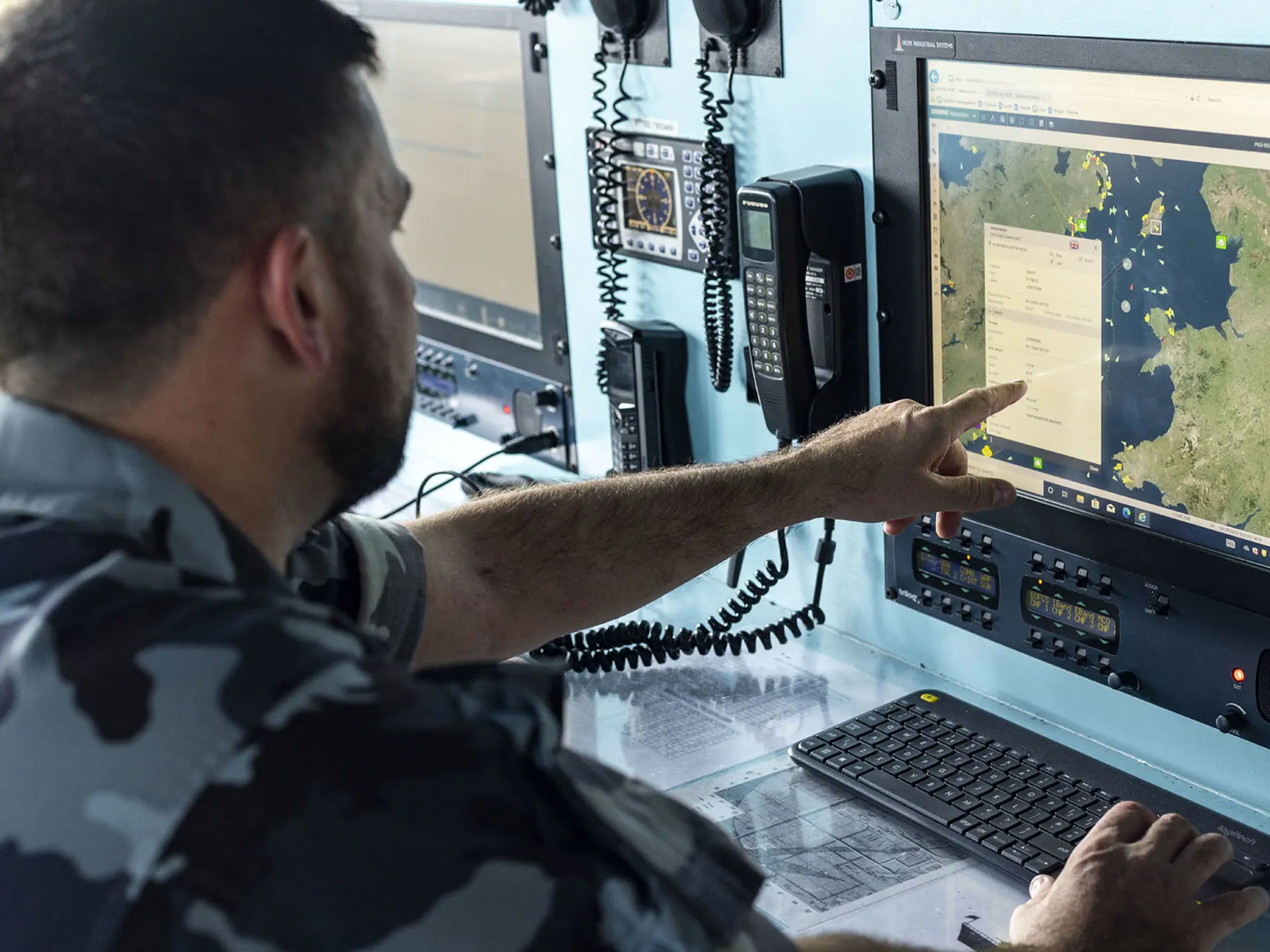 A naval officer in camouflage points at a maritime map on a computer screen in a command centre