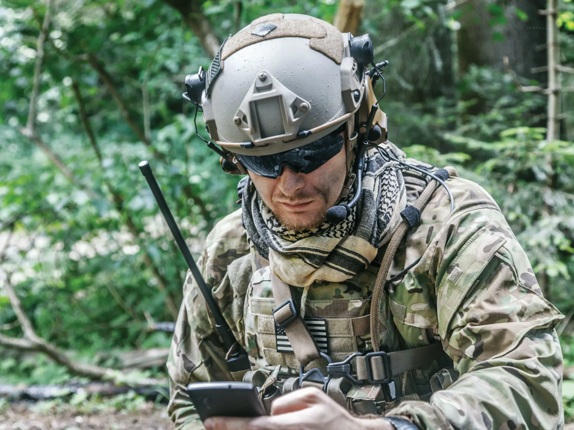 En soldat iført camouflage-taktisk udstyr og hjelm med monteret kamera kommunikerer via radio og tjekker en enhed i en tæt skov