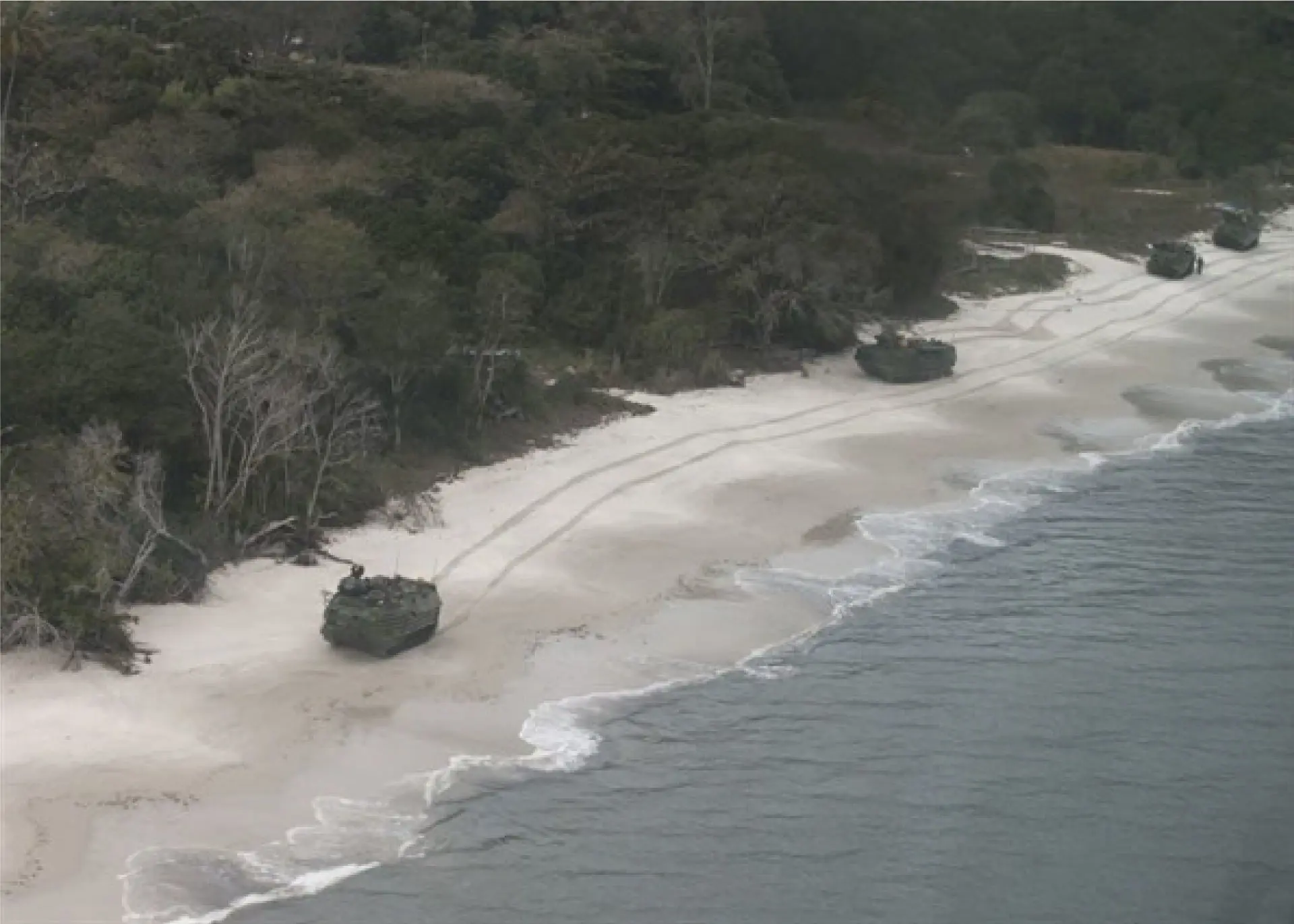 Multiple armoured vehicles driving on a shore. 