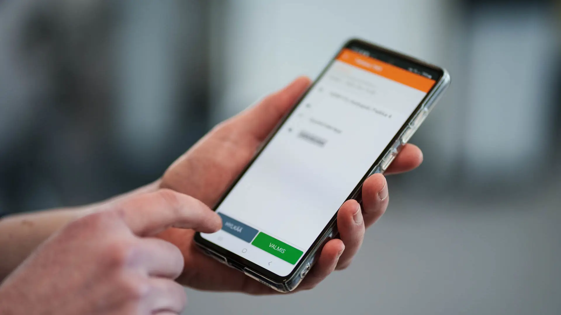 Person holding a mobile device displaying a task management system, captured in action just before tapping the screen.