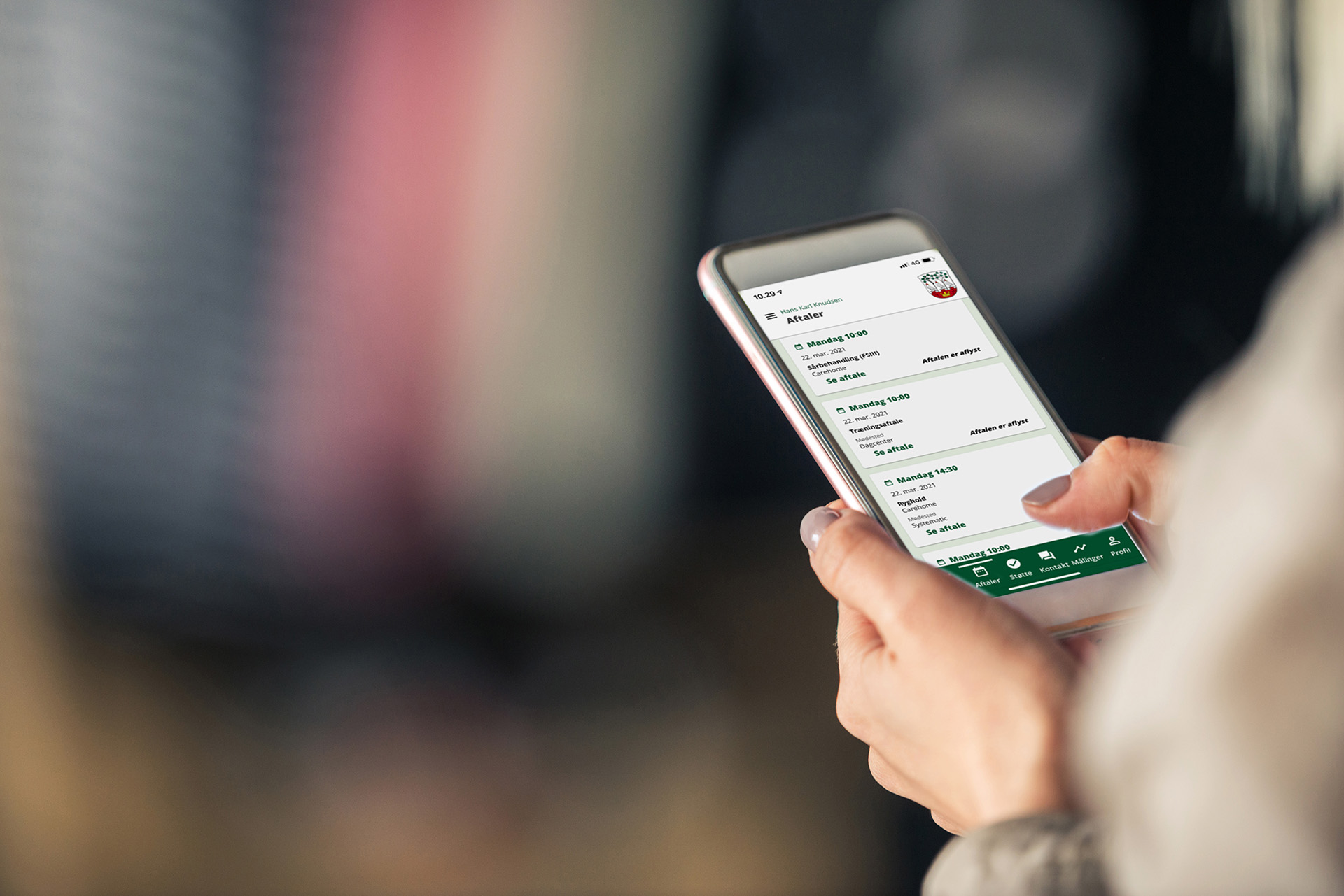Person holder en smartphone og tjekker planlagte aftaler i en kommunal app med grønt interface.