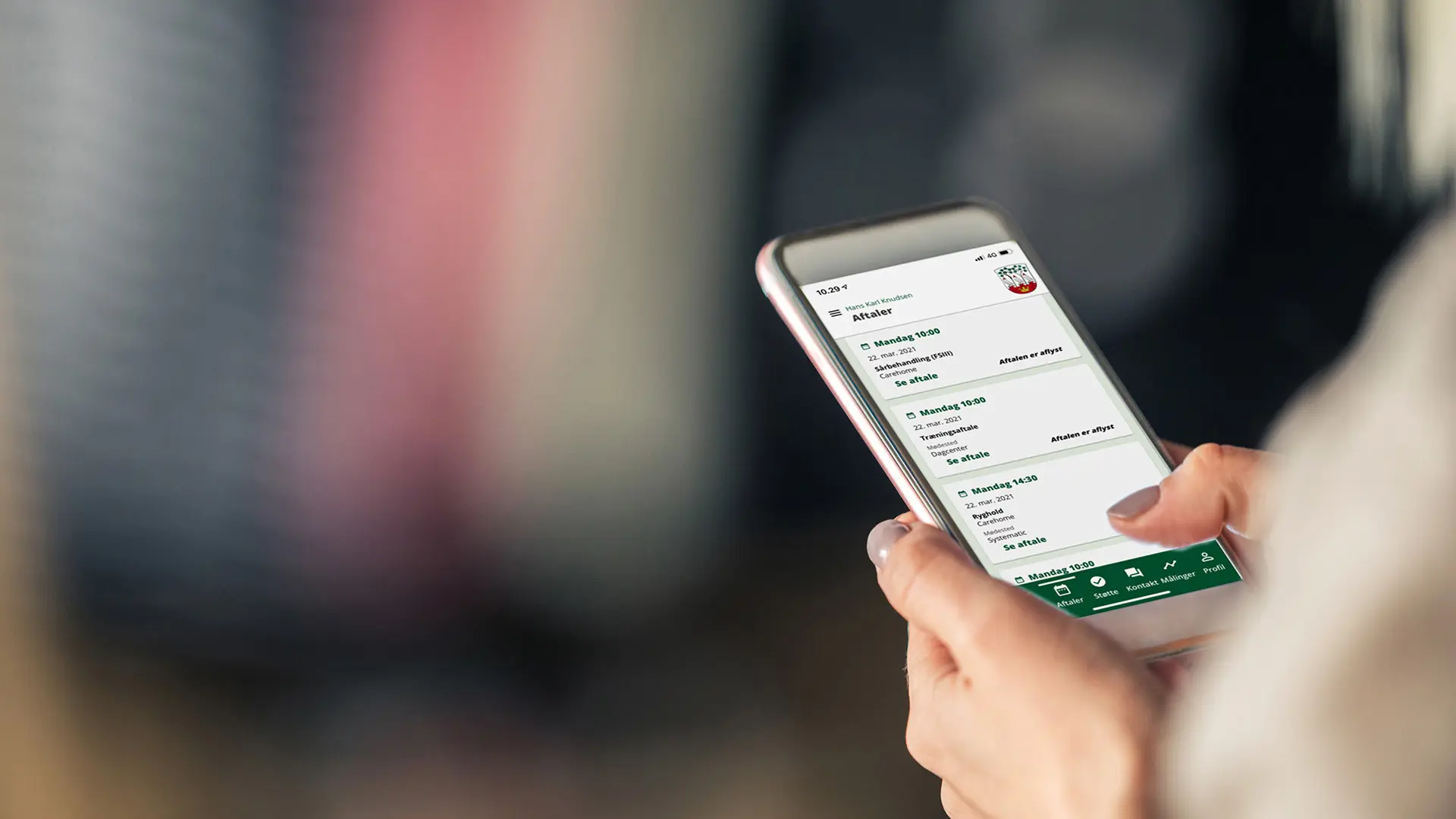 Person holding a smartphone and checking scheduled appointments in a Danish municipality app with a green interface