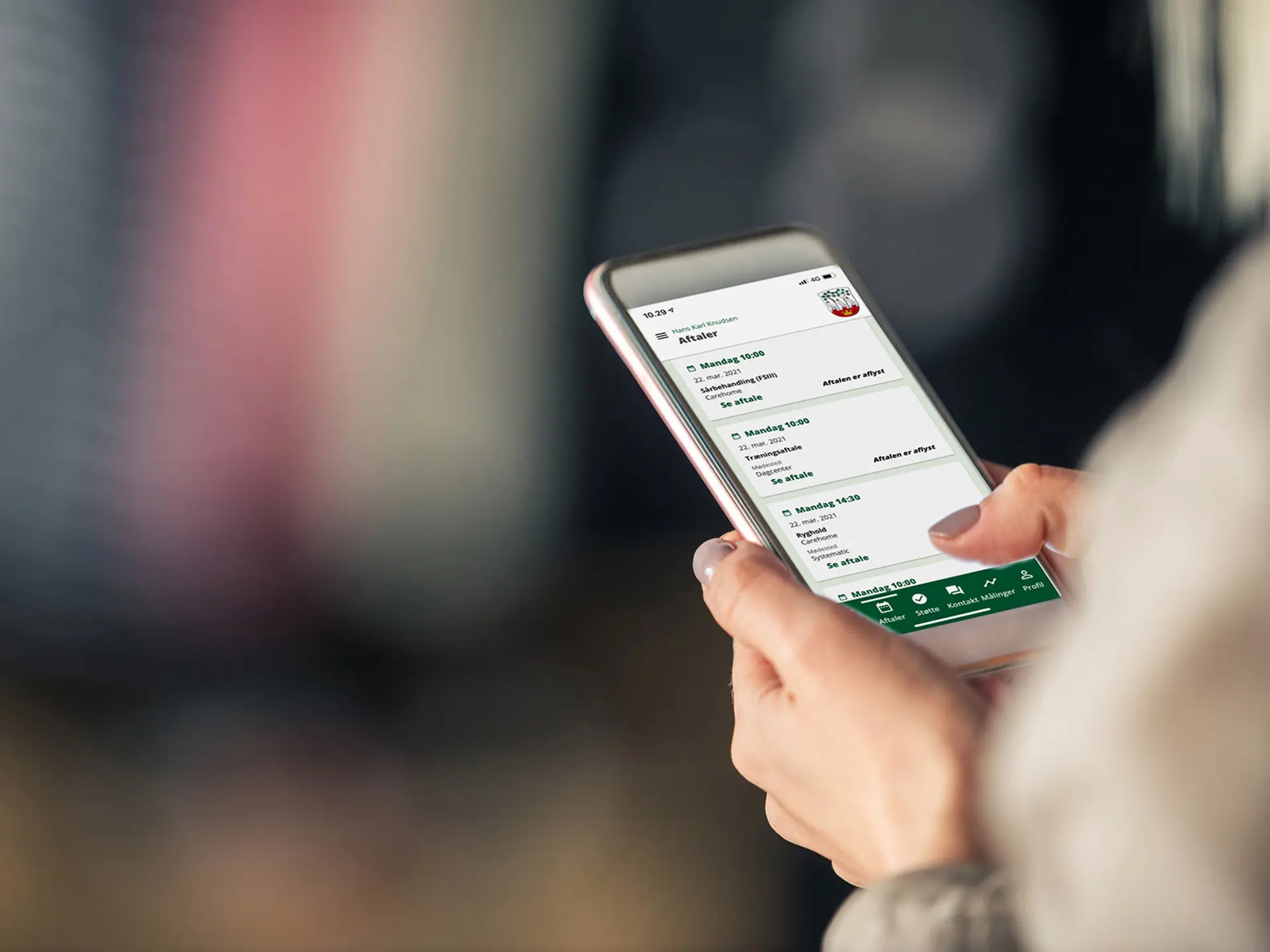 Person holder en smartphone og tjekker planlagte aftaler i en kommunal app med grønt interface.