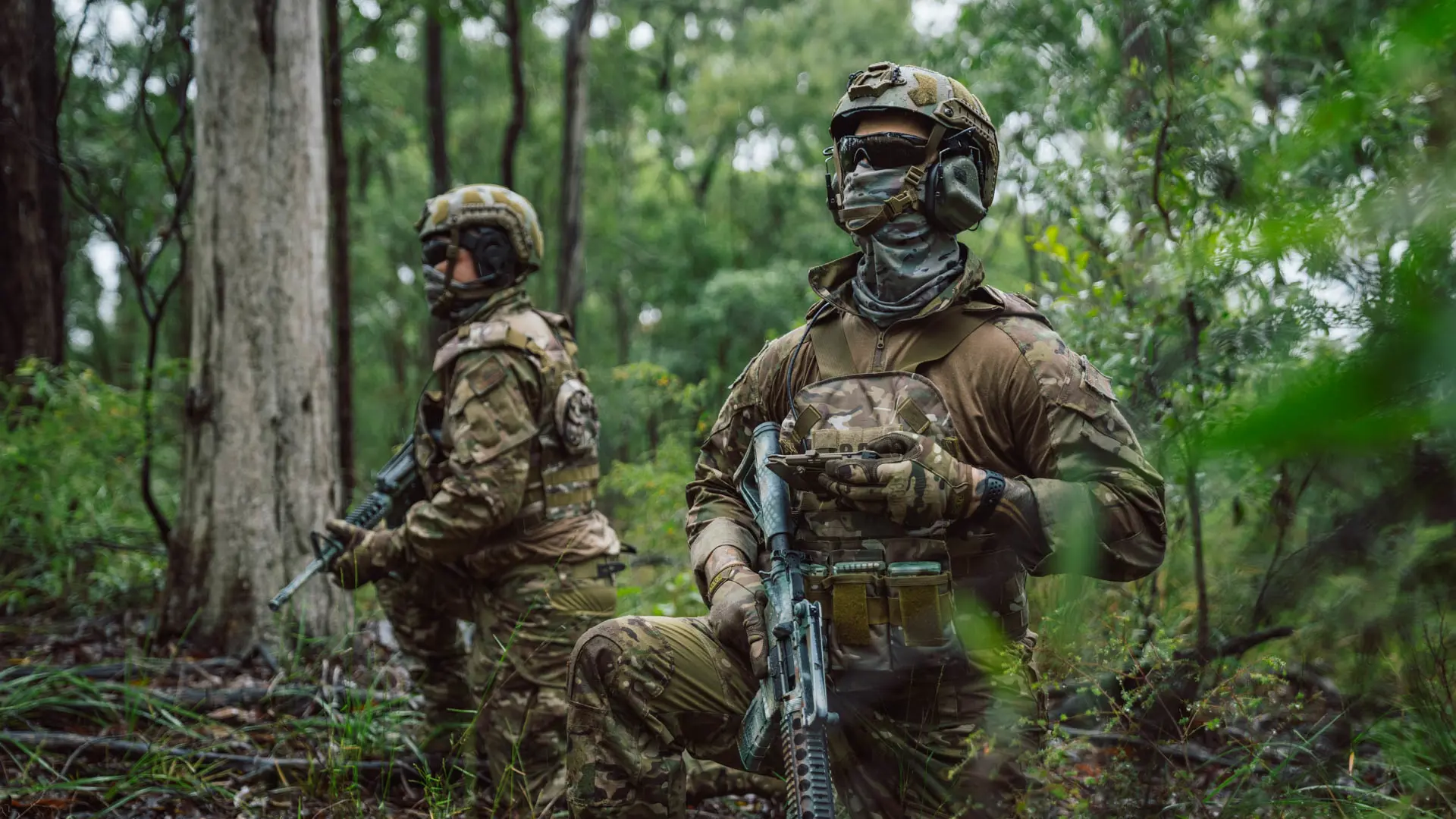 Soldiers kneeling in a woodland area using SitaWare Edge software for tactical communication.