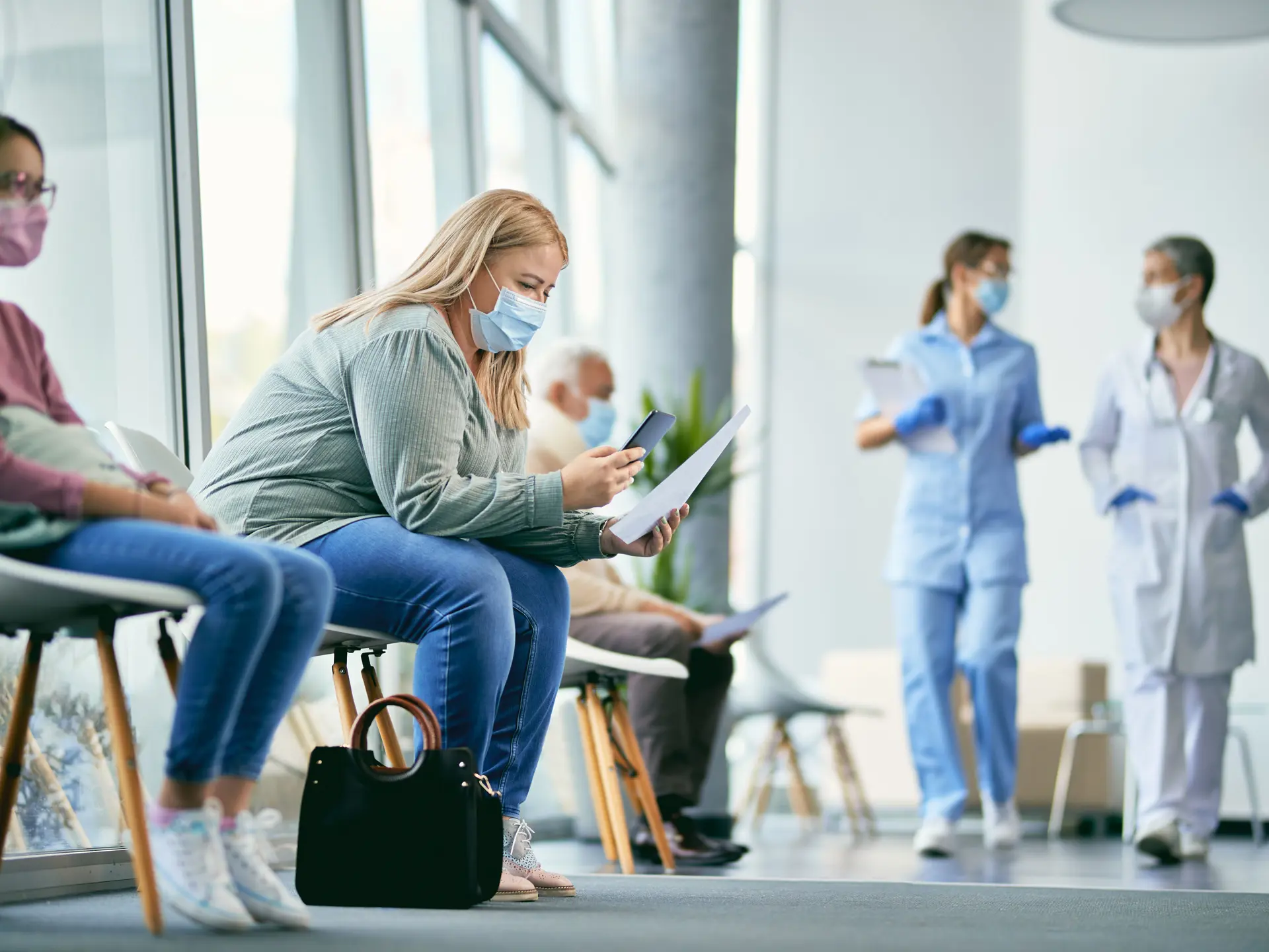 Kvindelig patient undersøger medicinske papirer og bruger mobiltelefon, mens hun sidder på gangen på hospitalet.