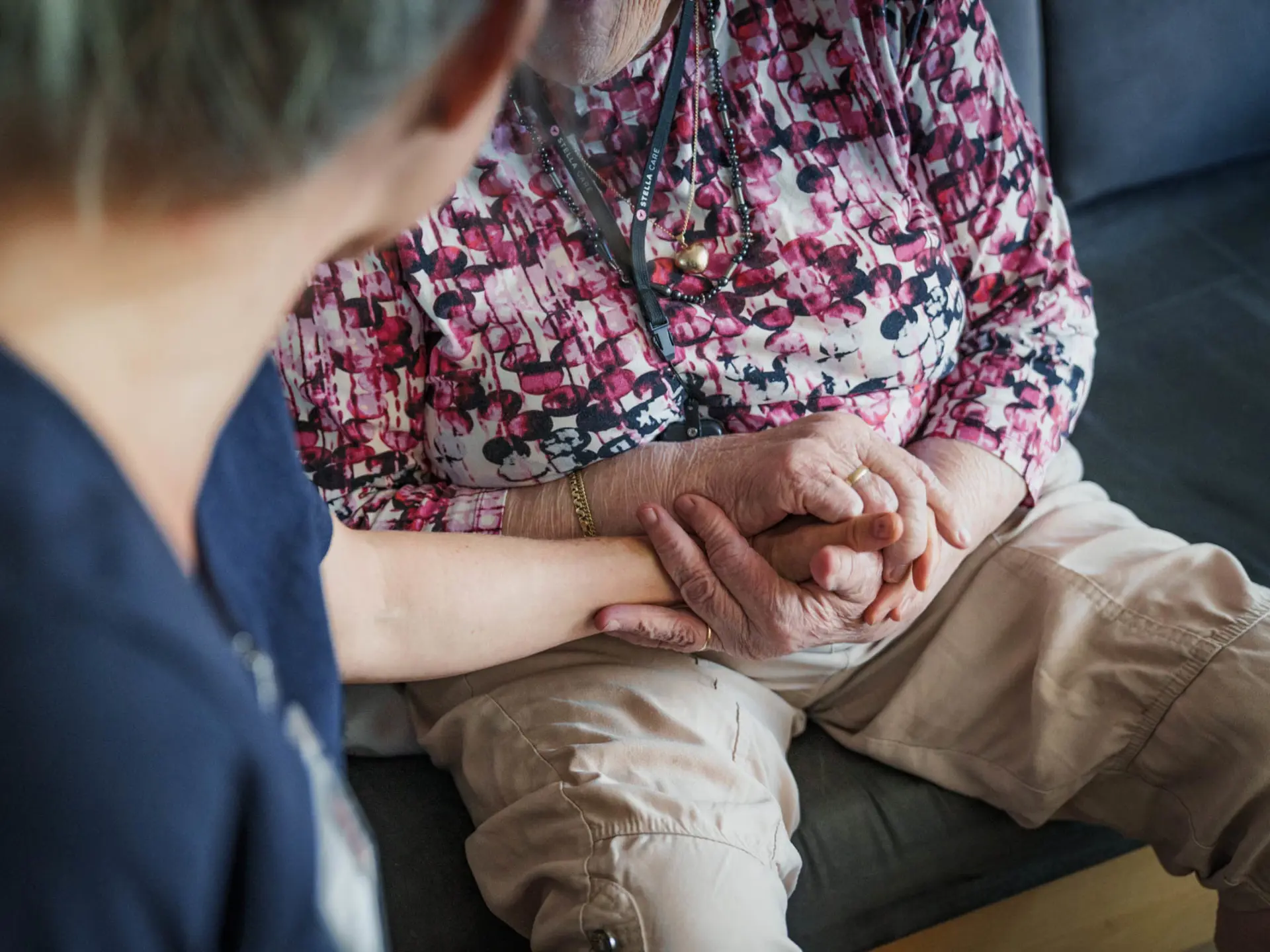 Social- og sundhedsassistent holder en borgers hånd i en støttende og omsorgsfuld gestus.