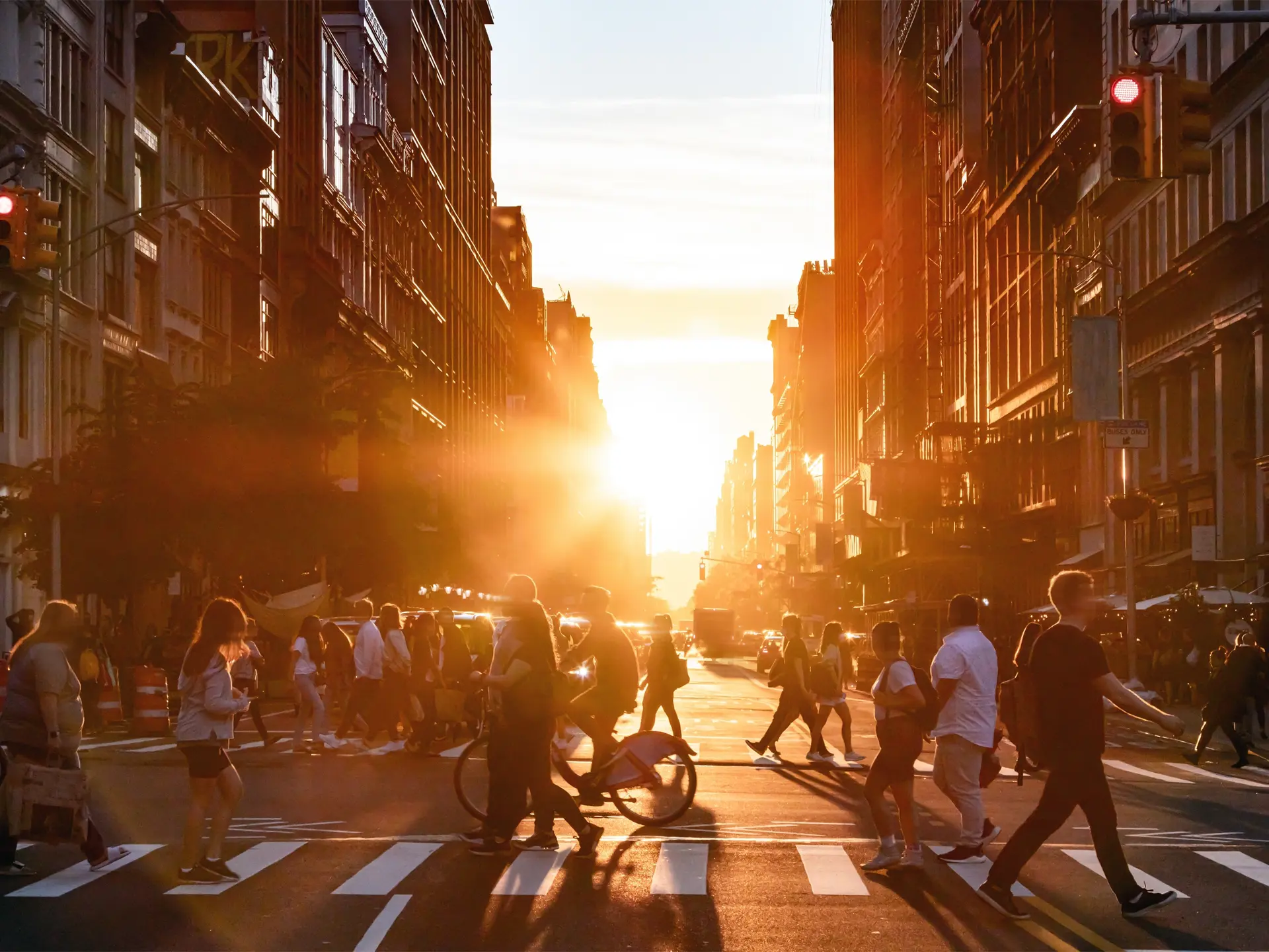 Busy city street at sunset with crowds of pedestrians and cyclists crossing the intersection between tall buildings.