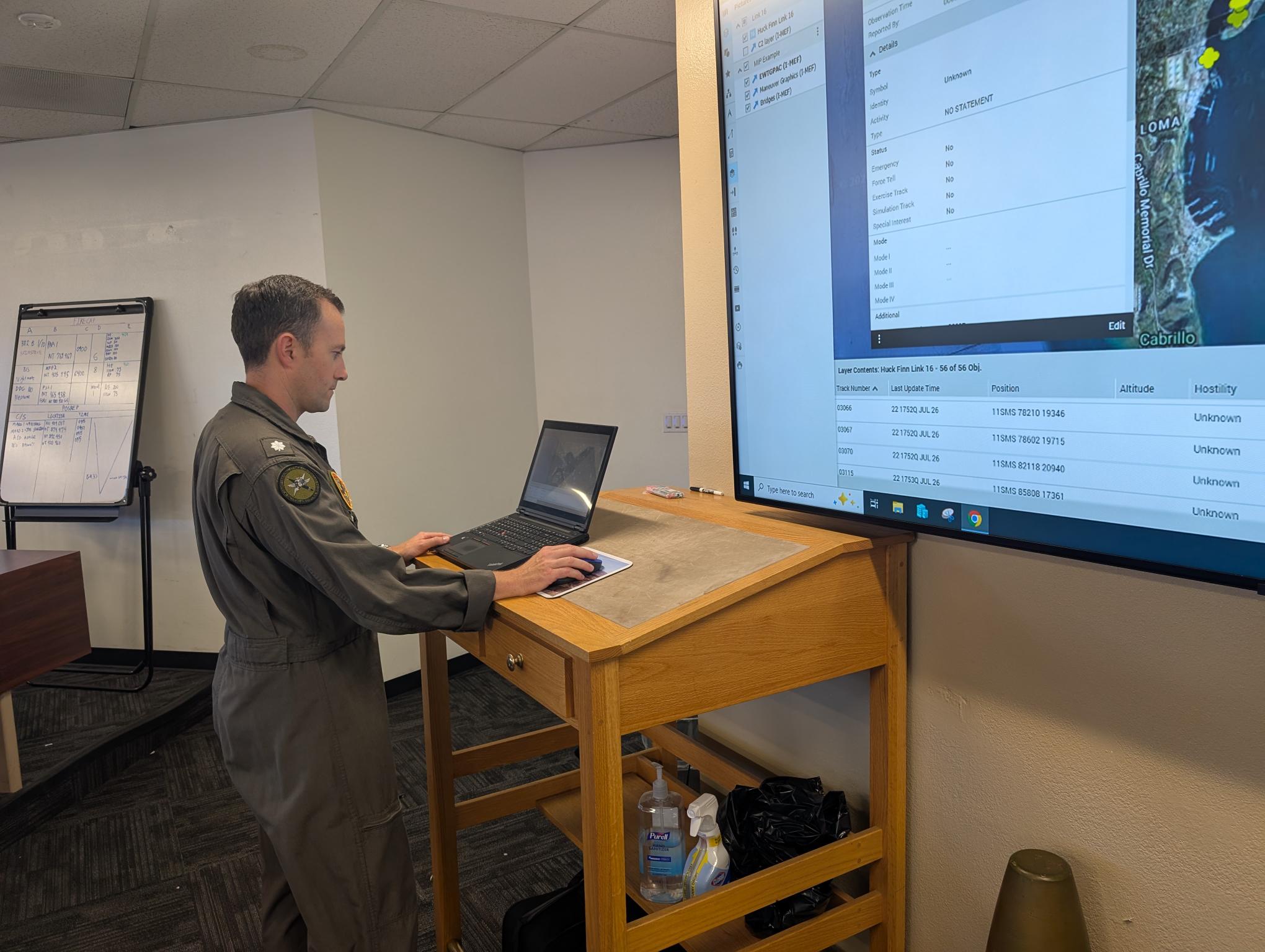 Military personnel uses a laptop while viewing a map and tactical track data in Systematic's SitaWare Headquarters on a large screen.