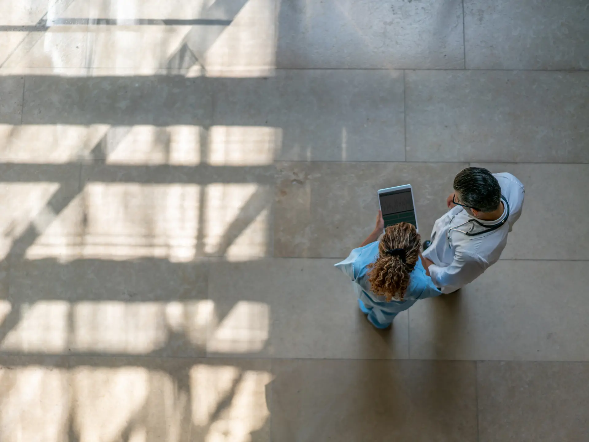 Nurse and doctor reviewing patient data on a tablet in a hospital hallway, supported by Columna Flow Suite for efficient hospital flow management.