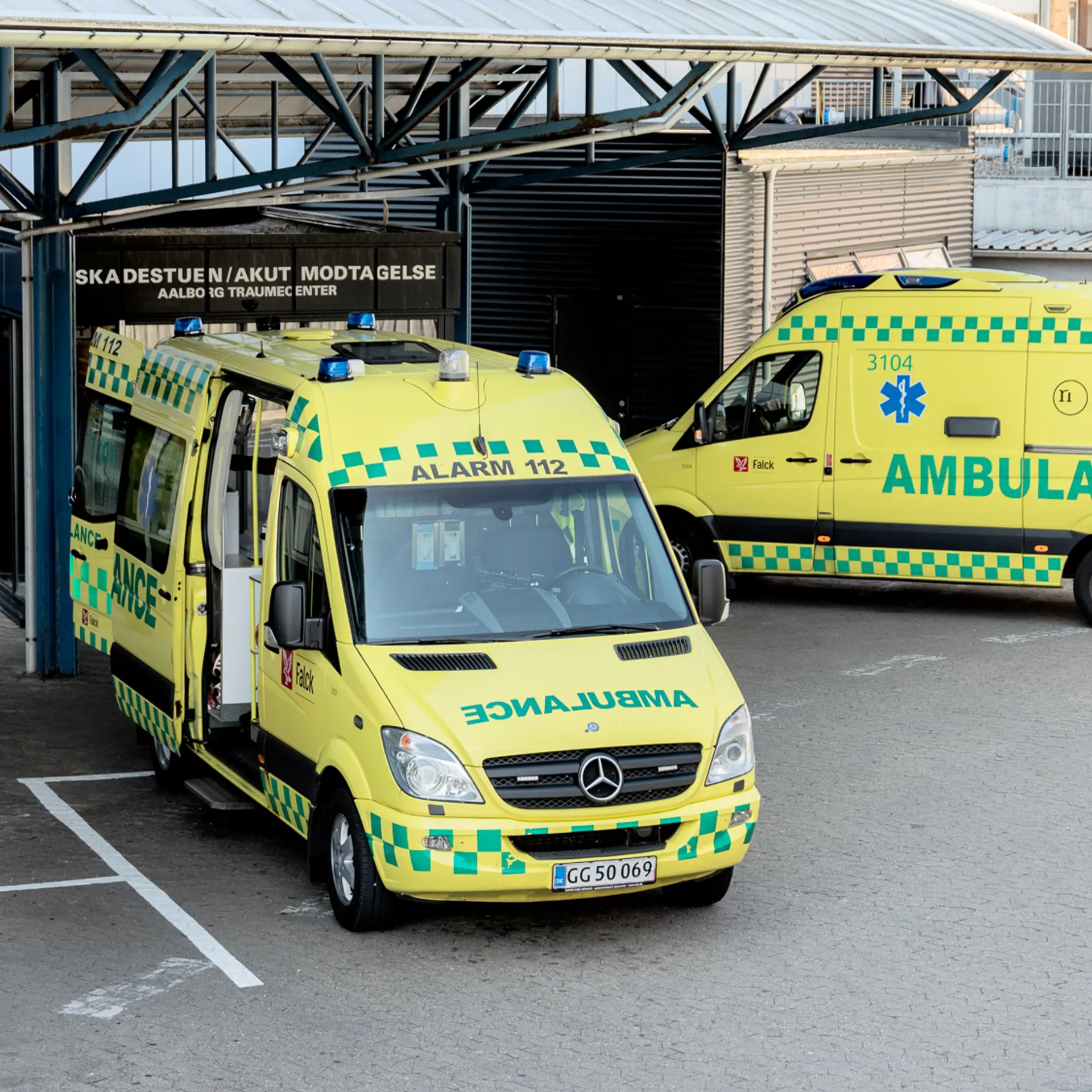 Two yellow ambulances parked outside a hospital emergency entrance, ready for patient transport and emergency medical response.