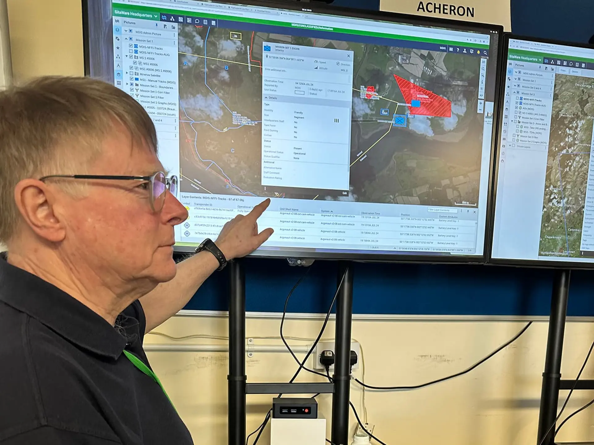 Man pointing at digital map on screen in an office setting, demonstrating software functionality.