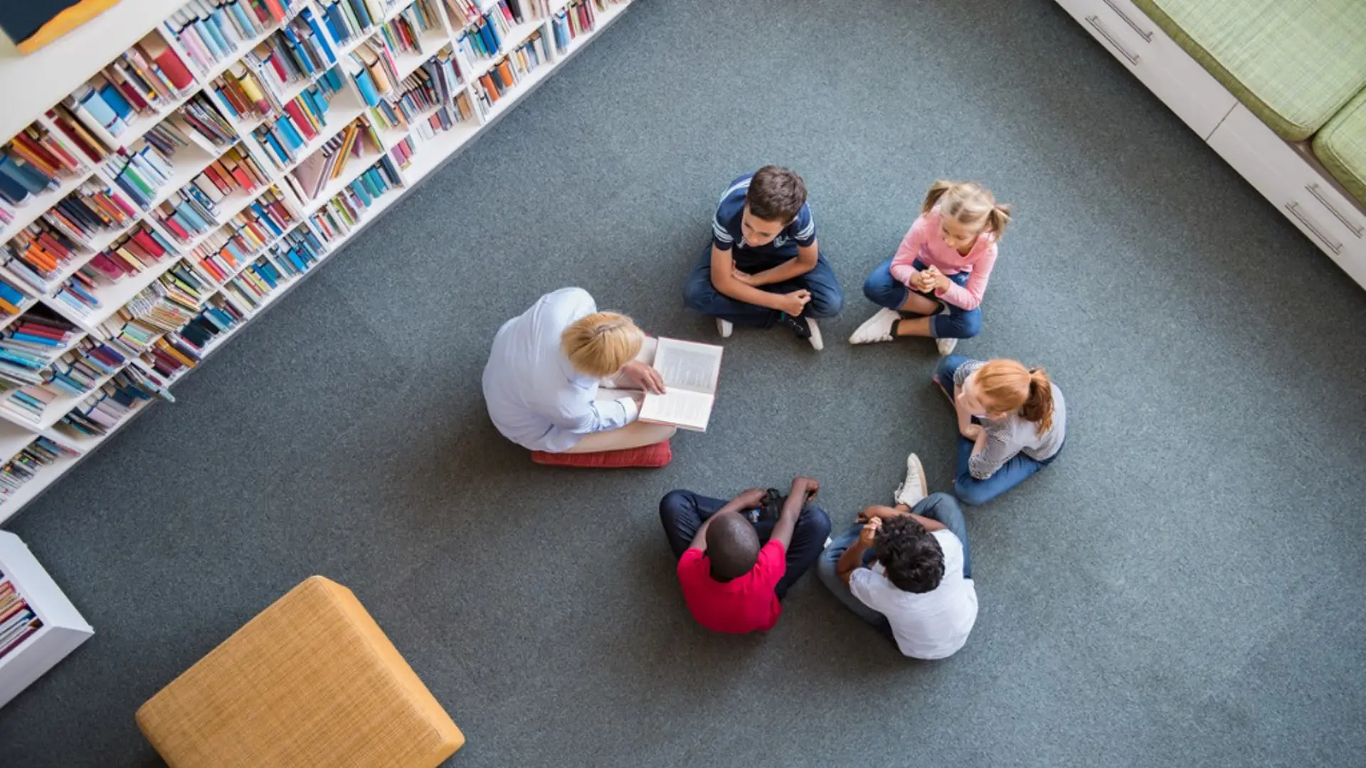 Children sitting in a circle lisiting to a librarian reading up a story