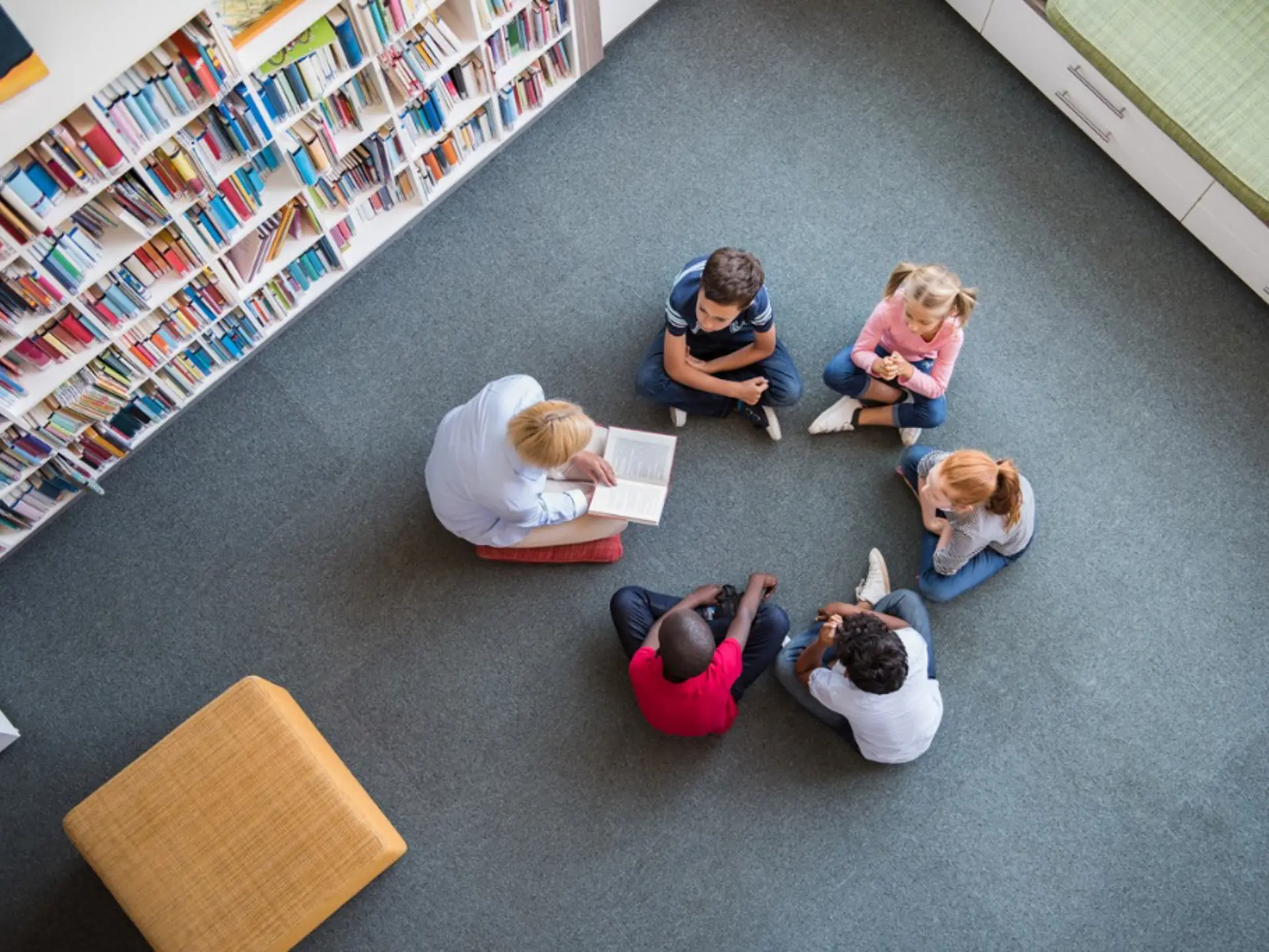 Children sitting in a circle lisiting to a librarian reading up a story
