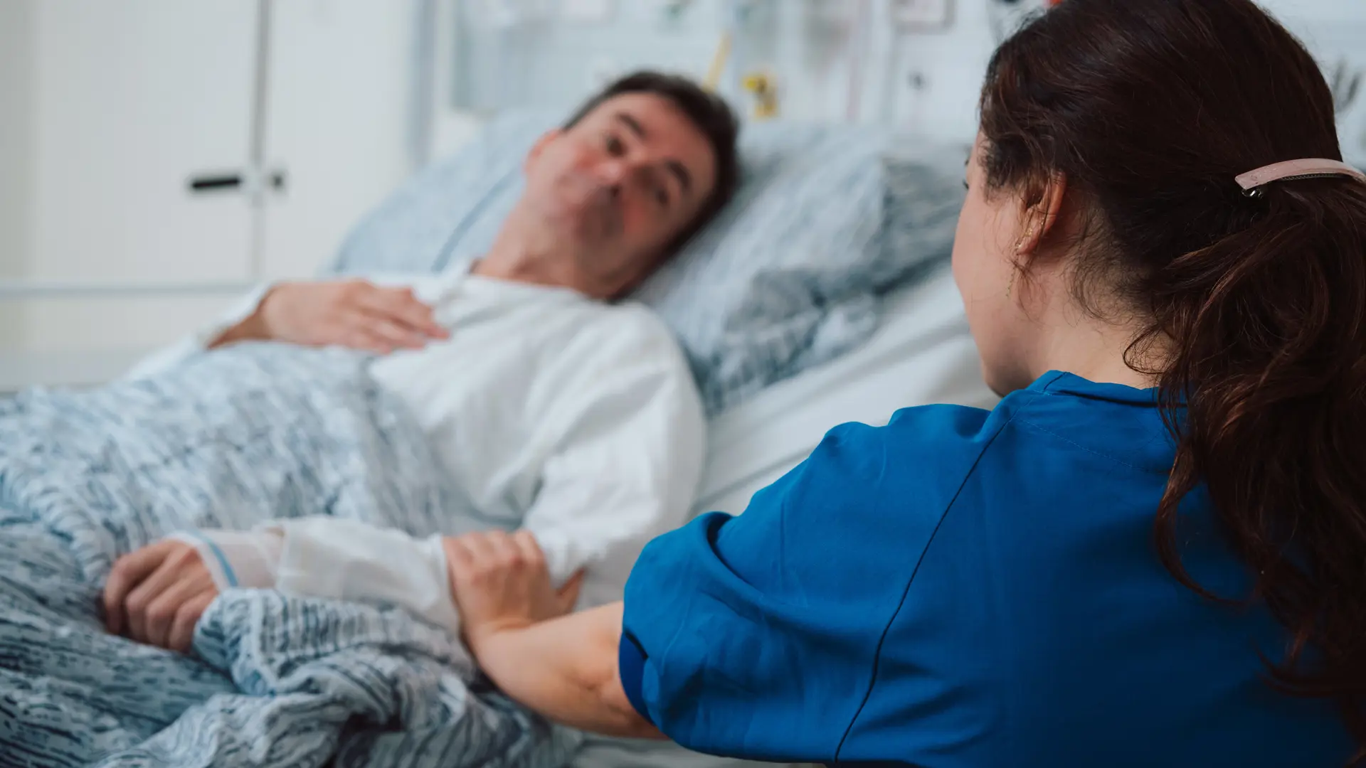 Nurse holding a hand on a bedridden patient