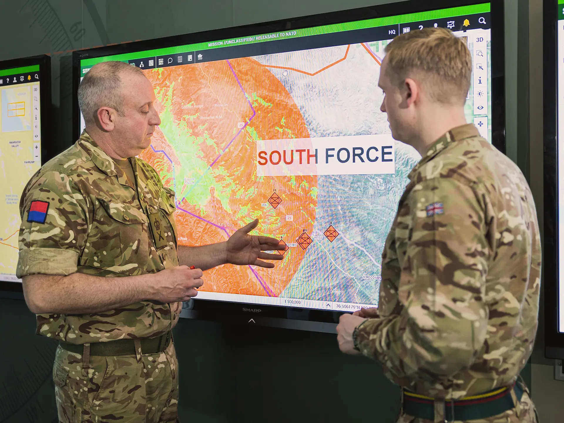 Military personnel talking in front of a screen