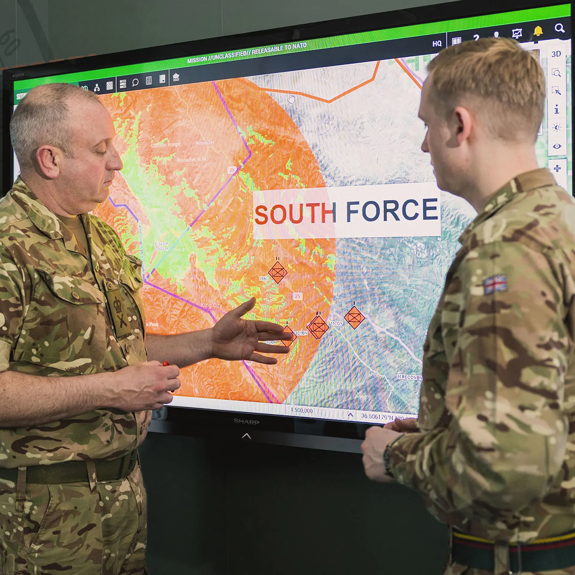 Military personnel talking in front of a screen