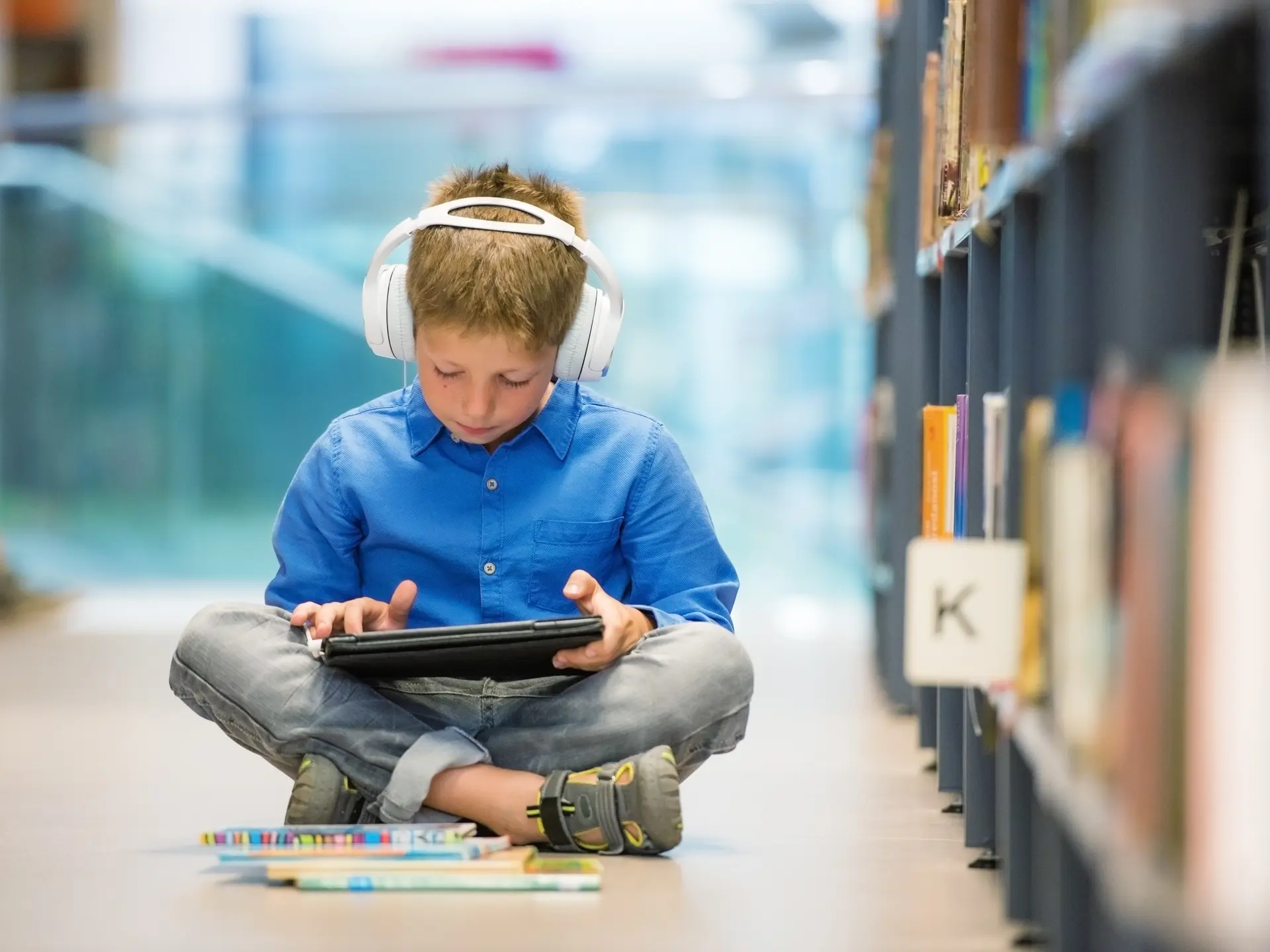 Dreng på gulvet i biblioteket med iPad og hovedtelefoner