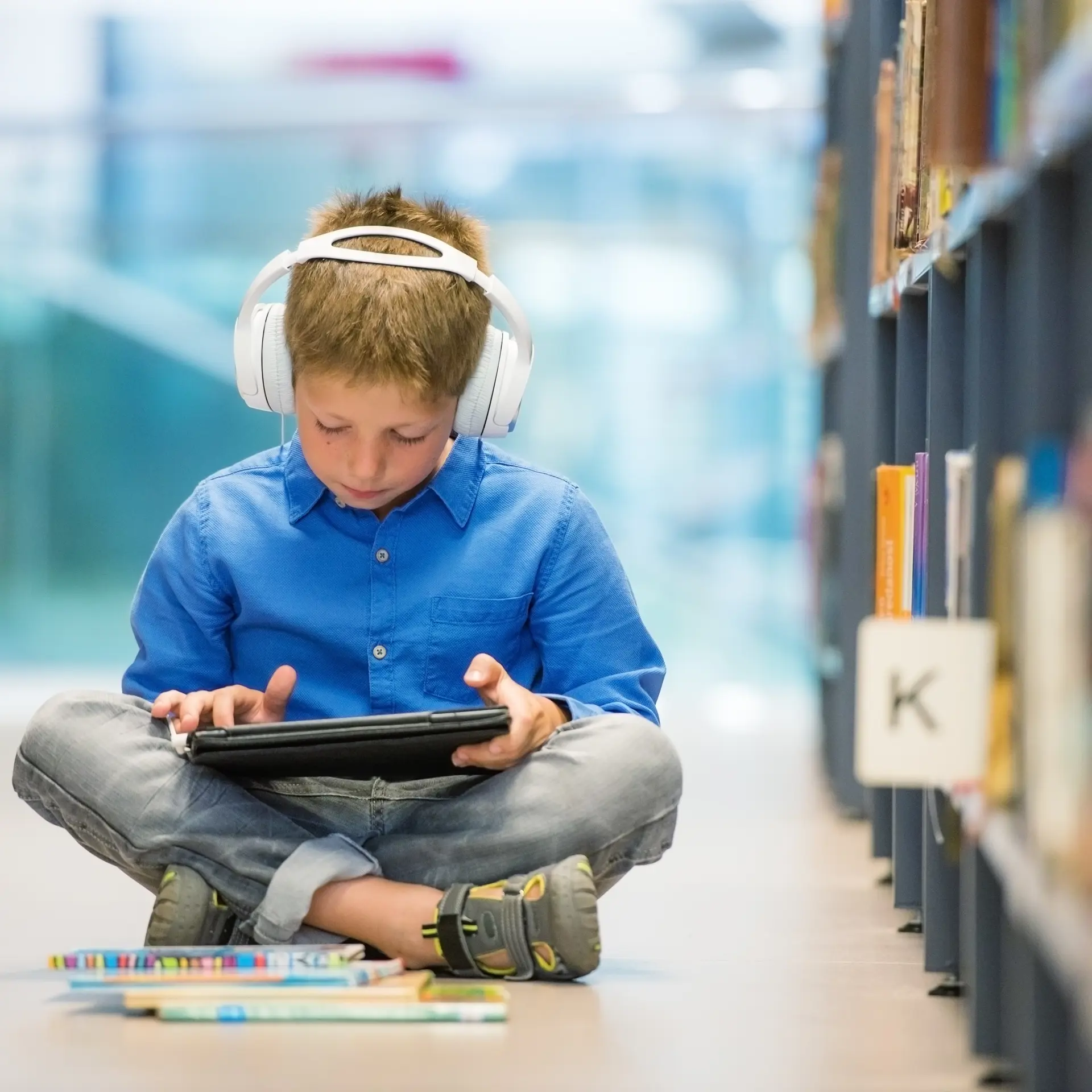 Dreng på gulvet i biblioteket med iPad og hovedtelefoner