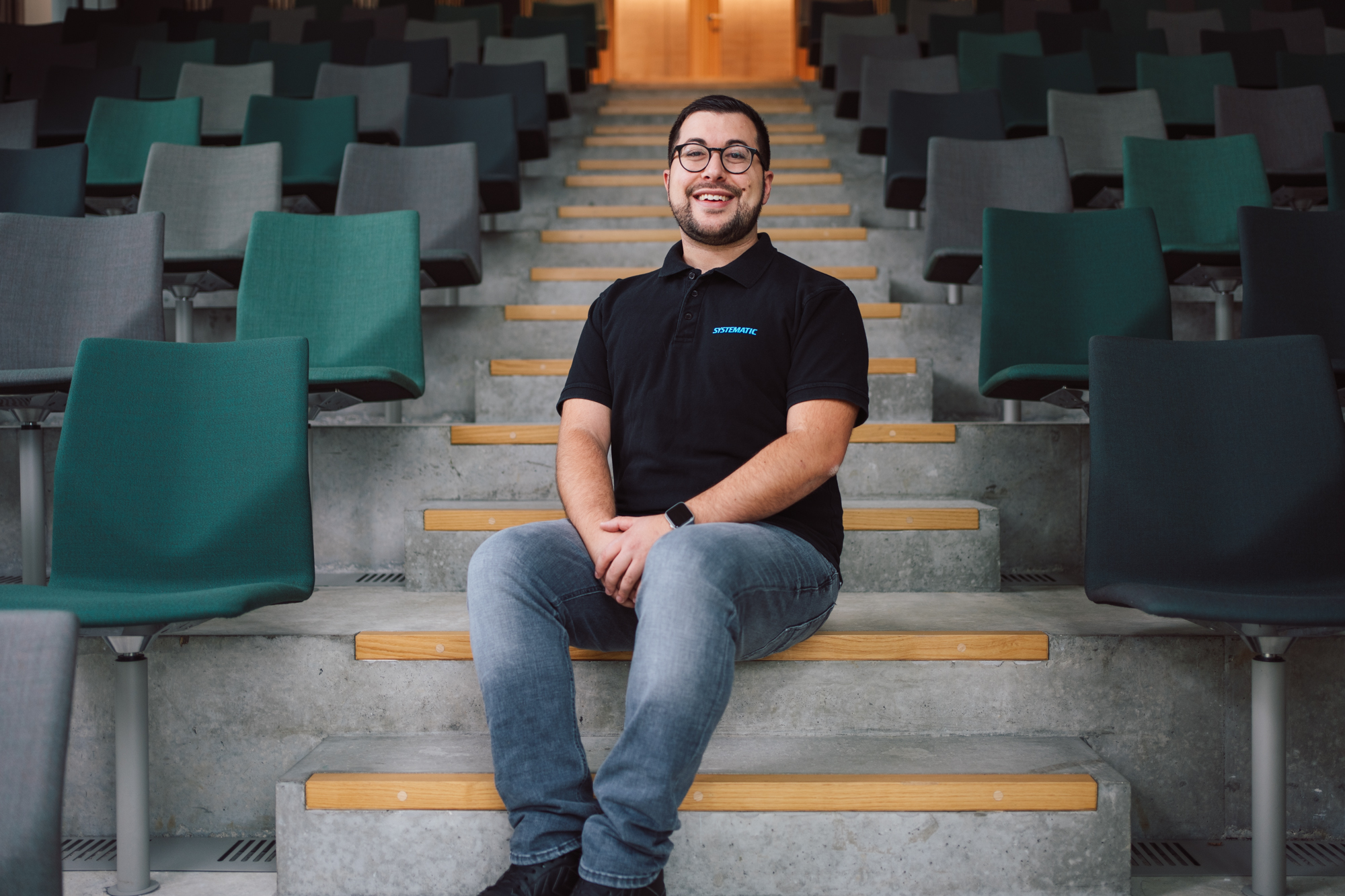 Thomas Vitale, Systematic employee, sitting on concrete steps in modern auditorium.