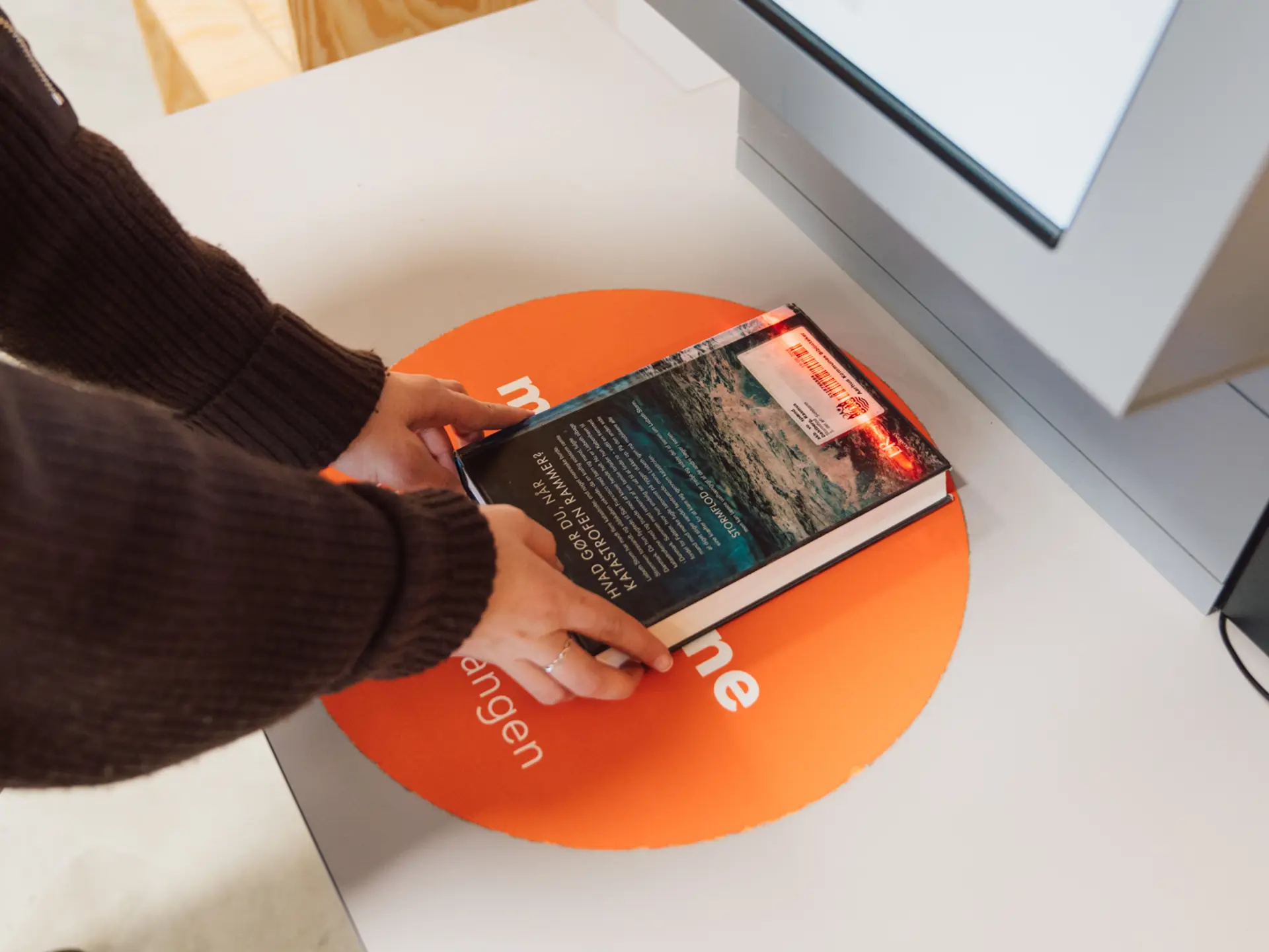A library user places a book on the scanning pad of a Cicero Slide self-service station as a red light reads the barcode.