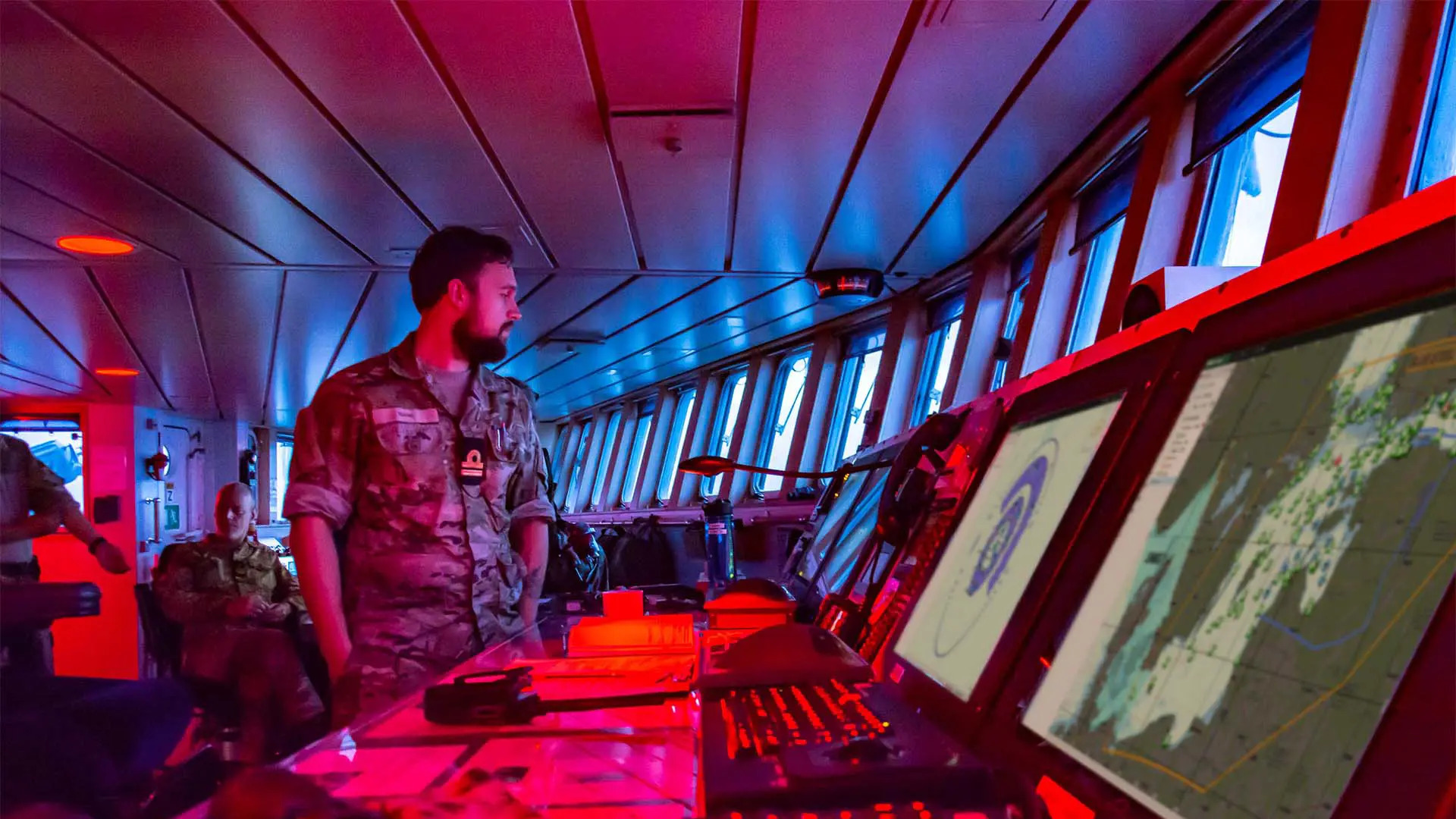 Naval commander overseeing ship bridge displays with SitaWare Maritime software to enhance situational awareness and operations.