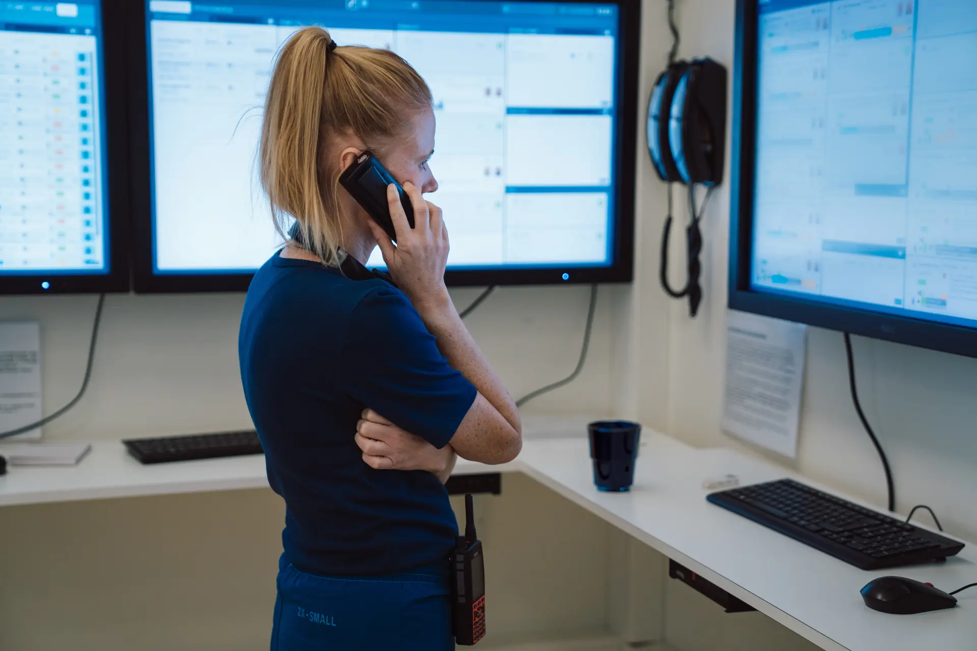 Healthcare professional talking on the phone at a workstation with multiple clinical software screens in a hospital setting.