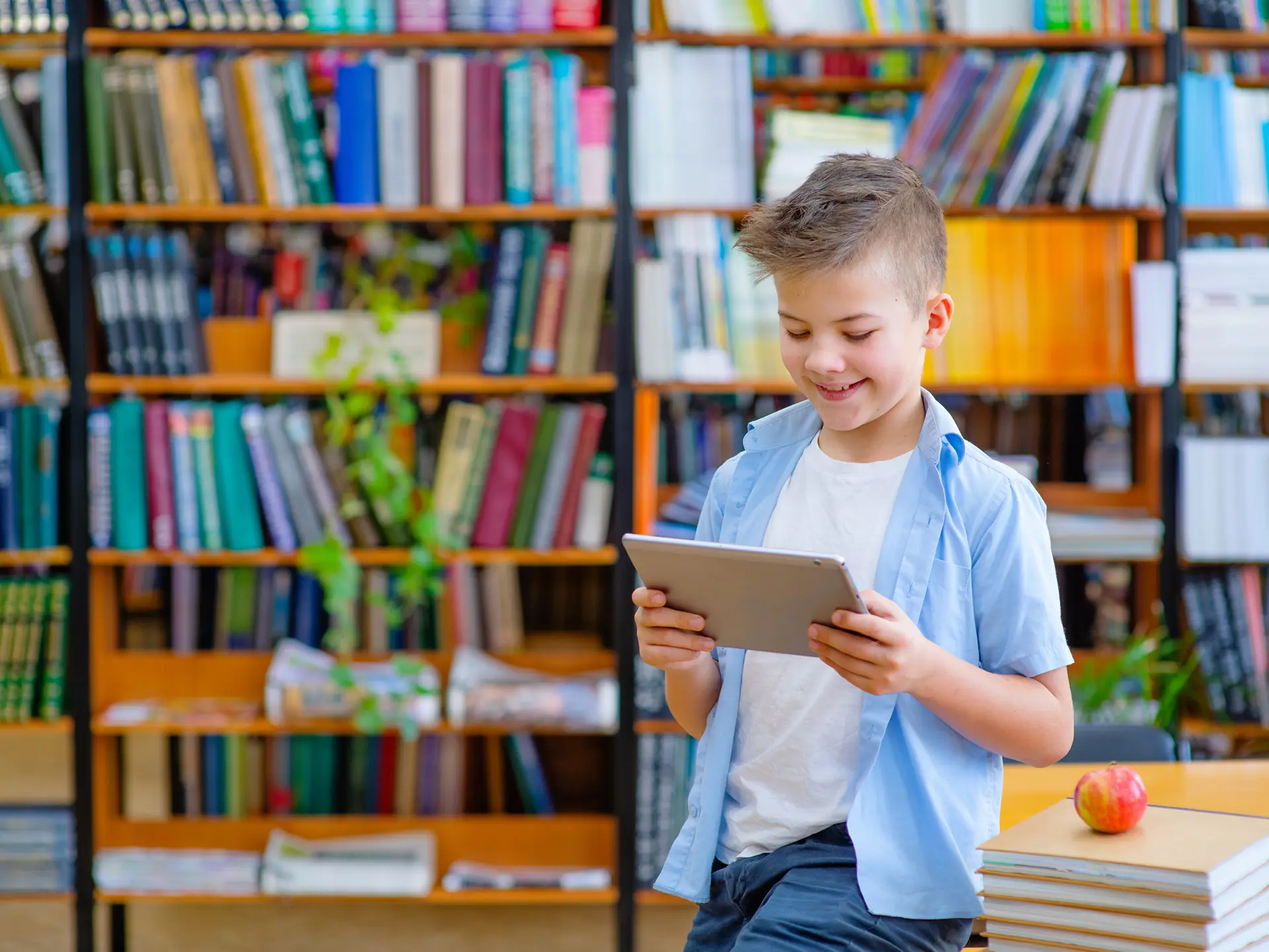 Pojke i blå skjorta med iPad i bibliotek