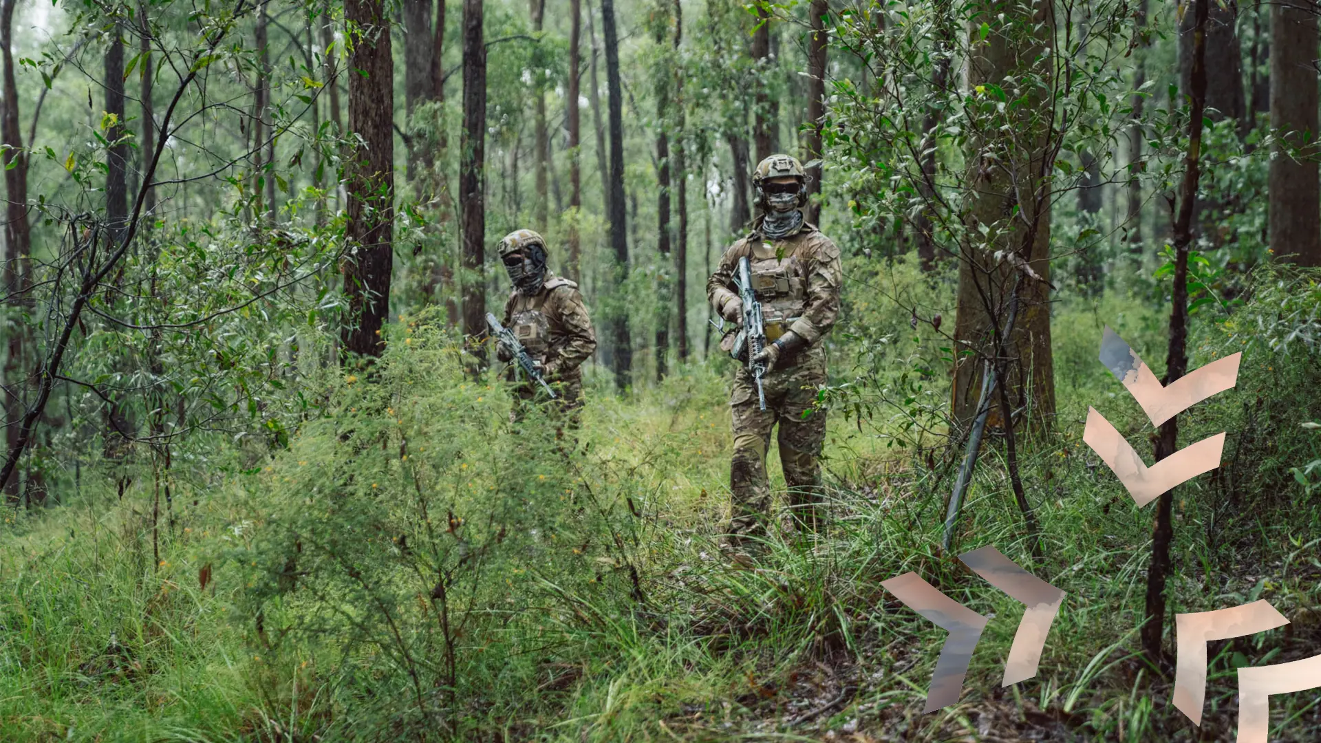 Two soldiers in camouflage patrol through dense forest with rifles, surrounded by tall trees and undergrowth.