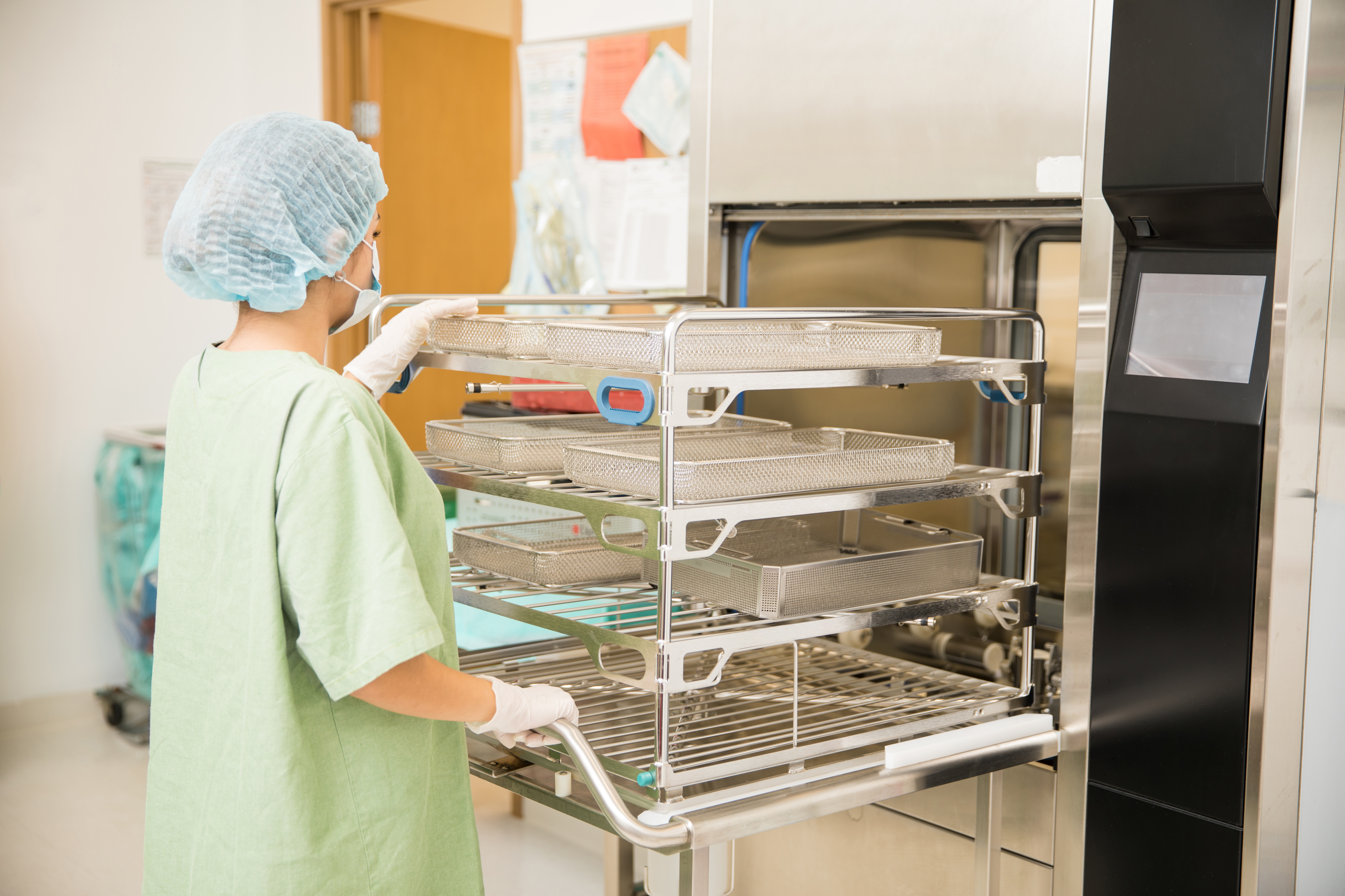 Healthcare professional in scrubs loading trays of medical instruments into a sterilisation unit