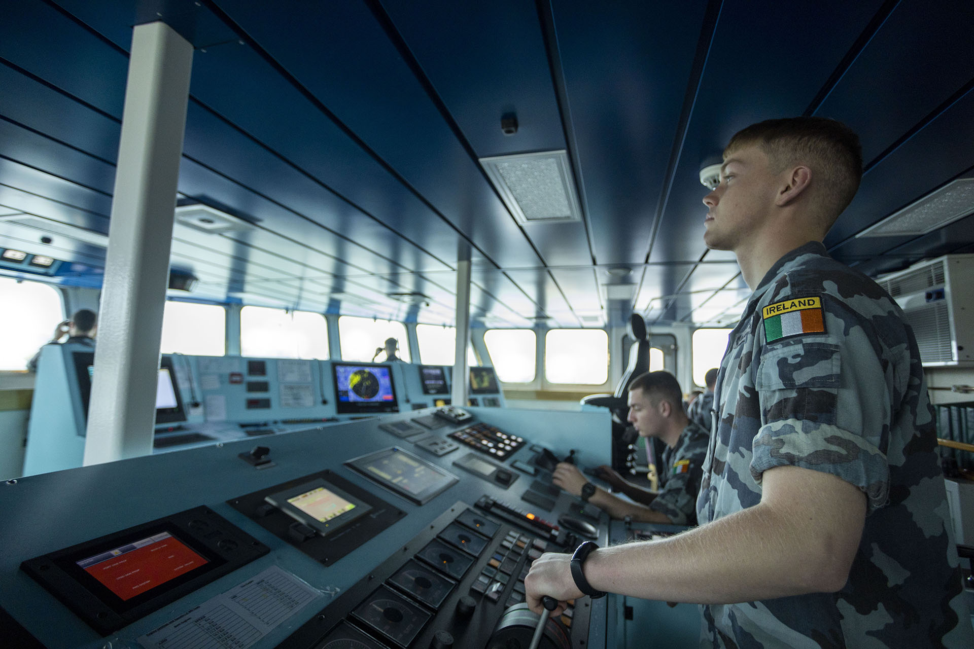 Naval officers operating navigation and communication systems on a ship’s bridge, monitoring radar and control panels during maritime operations.
